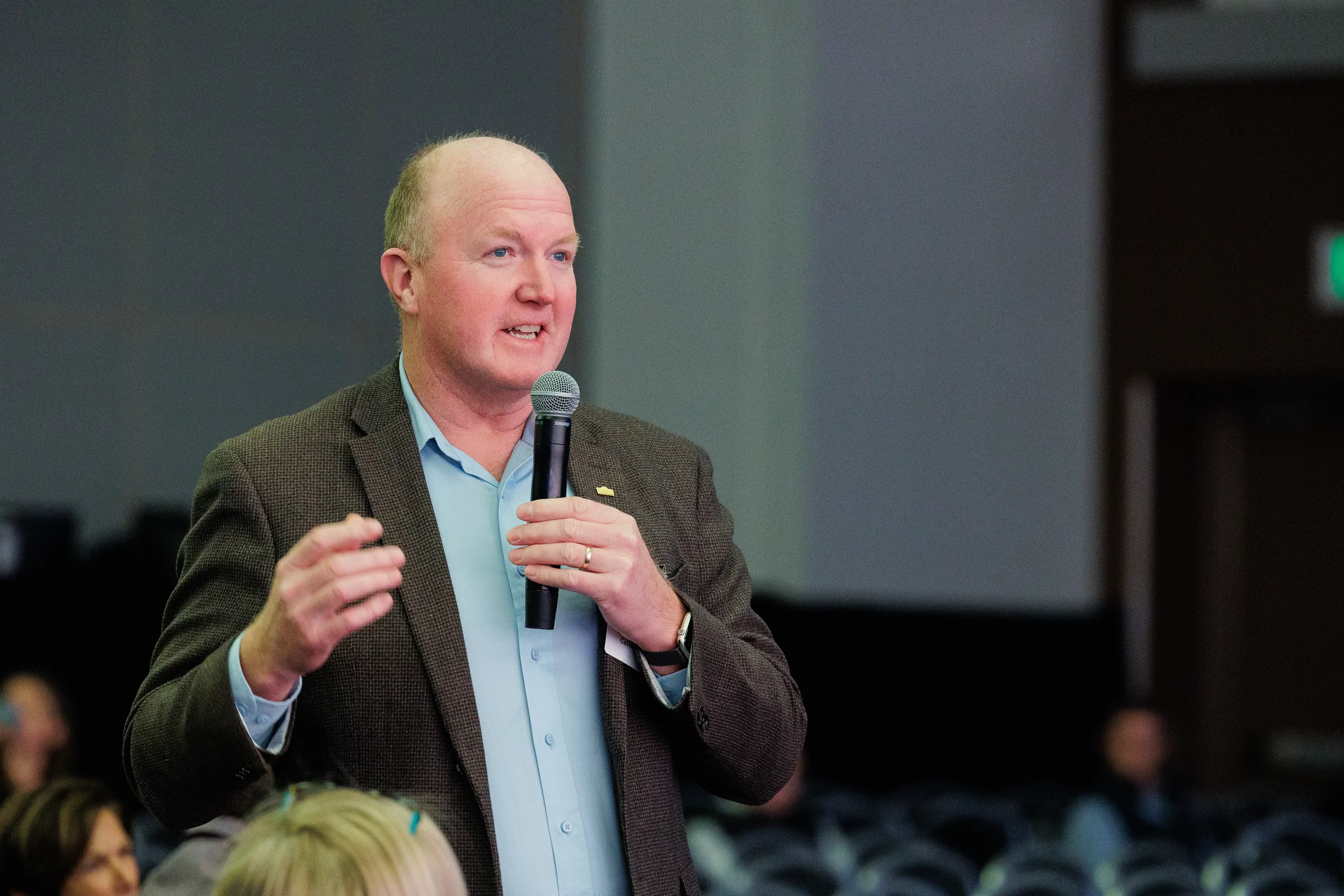 Badged attendee stands with microphone gesturing while speaking during Orlando corporate conference session