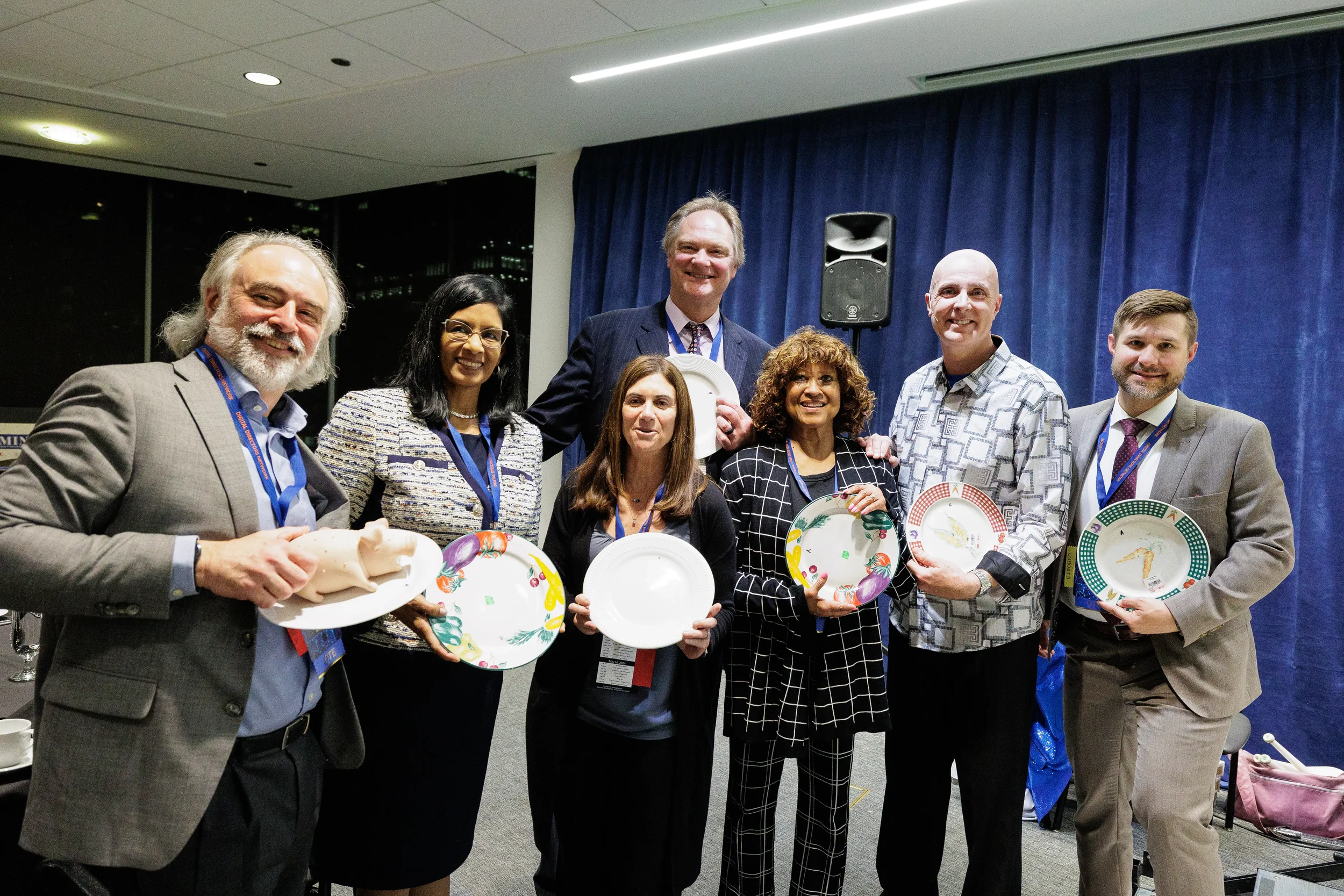 Group of seven attendees with lanyards hold decorated plates on stage at Chicago industry conference