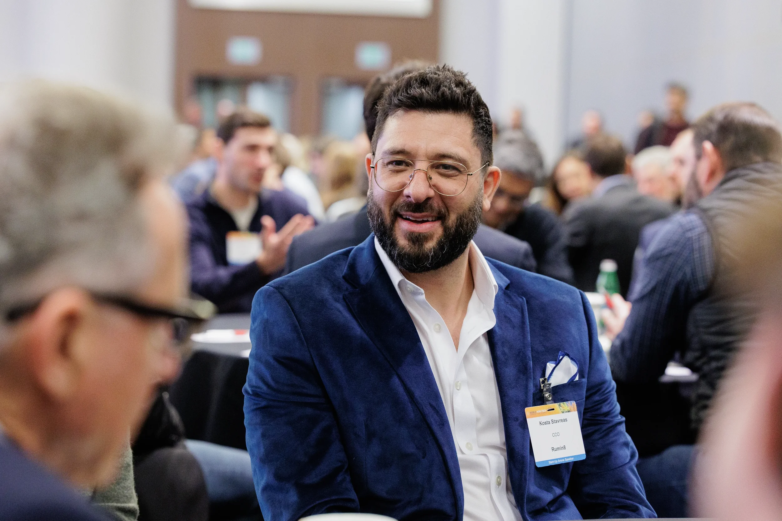 Smiling badged attendee in navy blazer at table during networking session at Chicago corporate conference