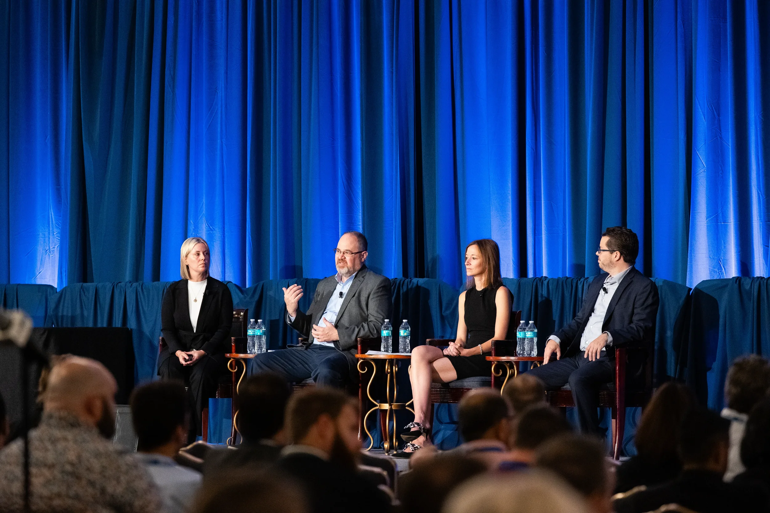 Four panelists seated on stage before blue drape backdrop address audience at Chicago industry conference