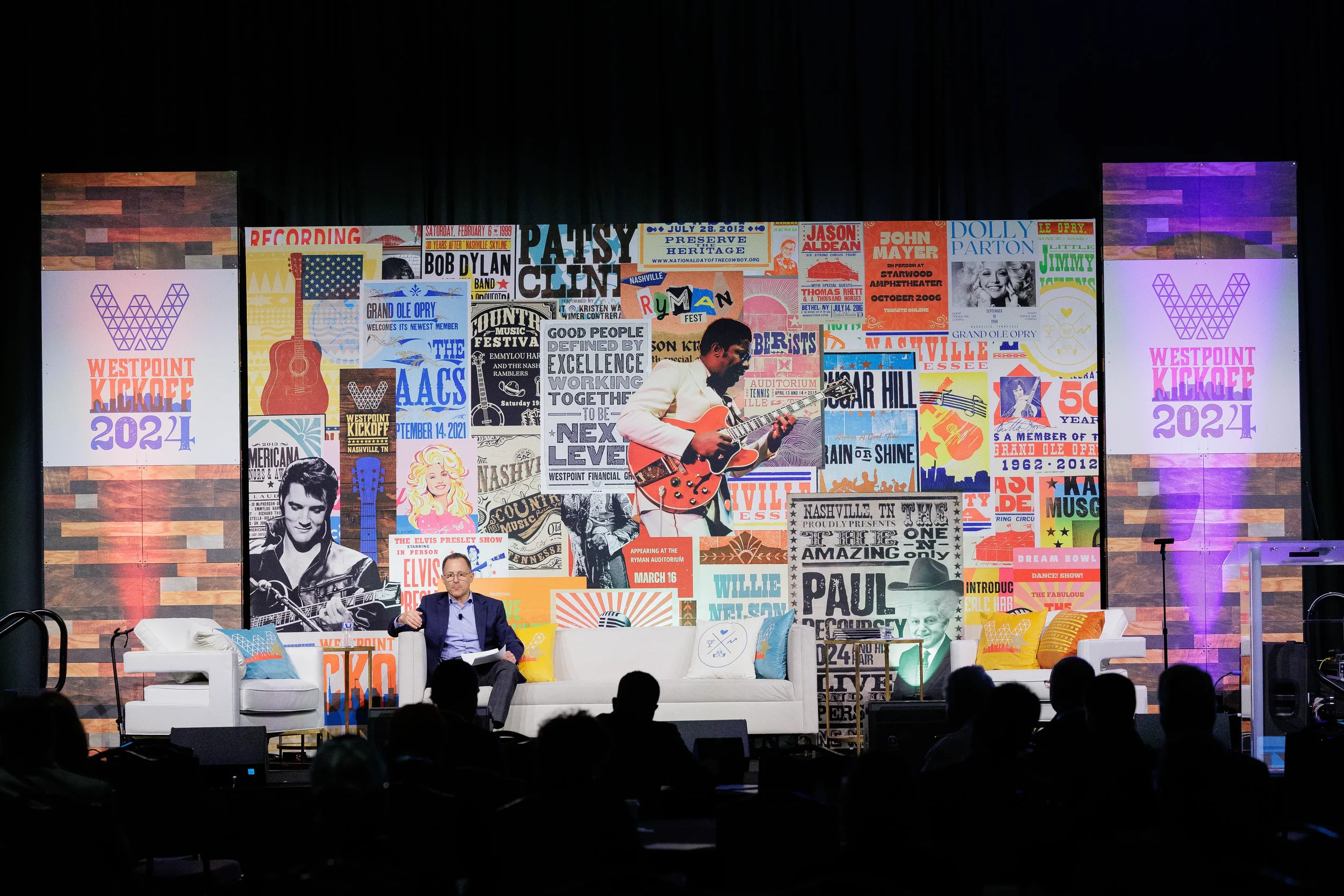 one speaker seated on stage in front of large branded backdrop before audience at Orlando corporate conference
