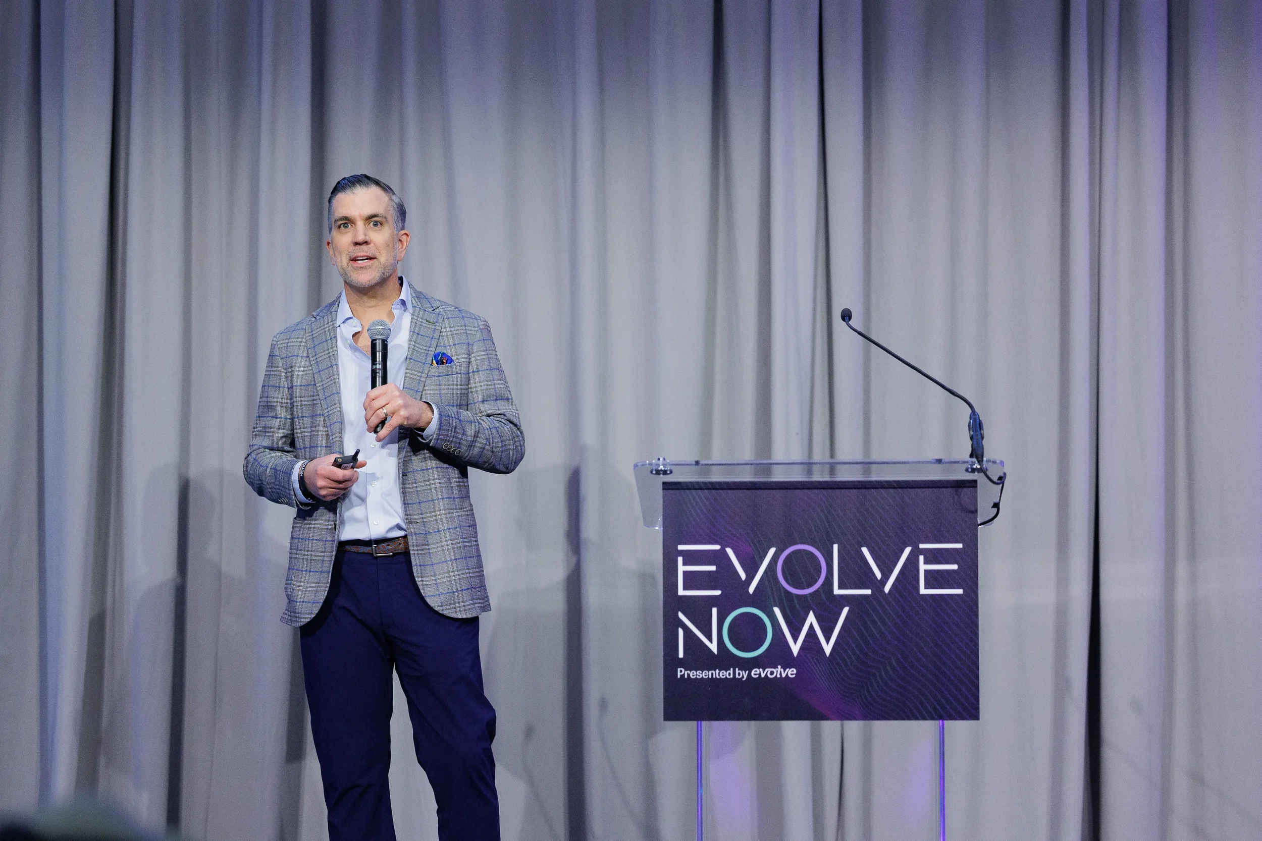 Speaker in plaid blazer presents on stage beside branded podium at Orlando corporate event