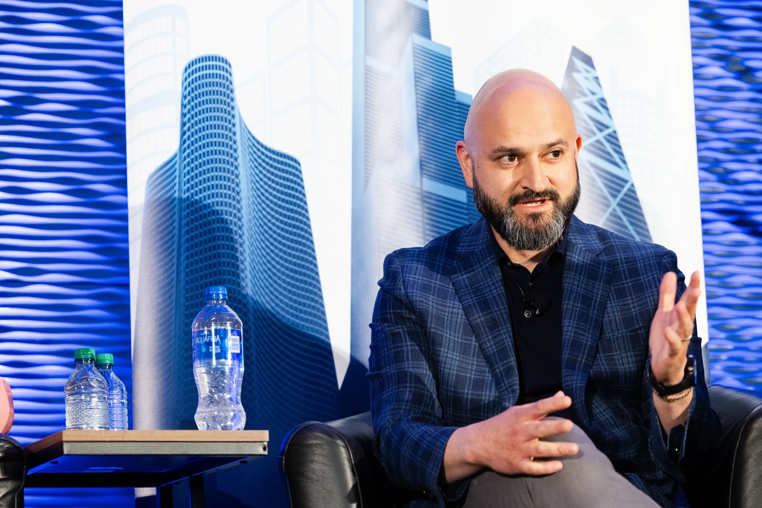 Panelist gestures while speaking on stage with skyline backdrop at Chicago corporate conference