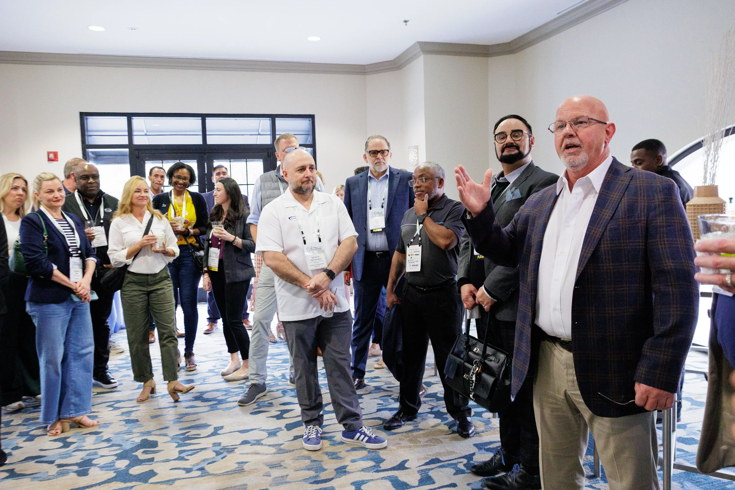 Speaker with raised hand addresses large group of attendees in foyer at Orlando corporate conference