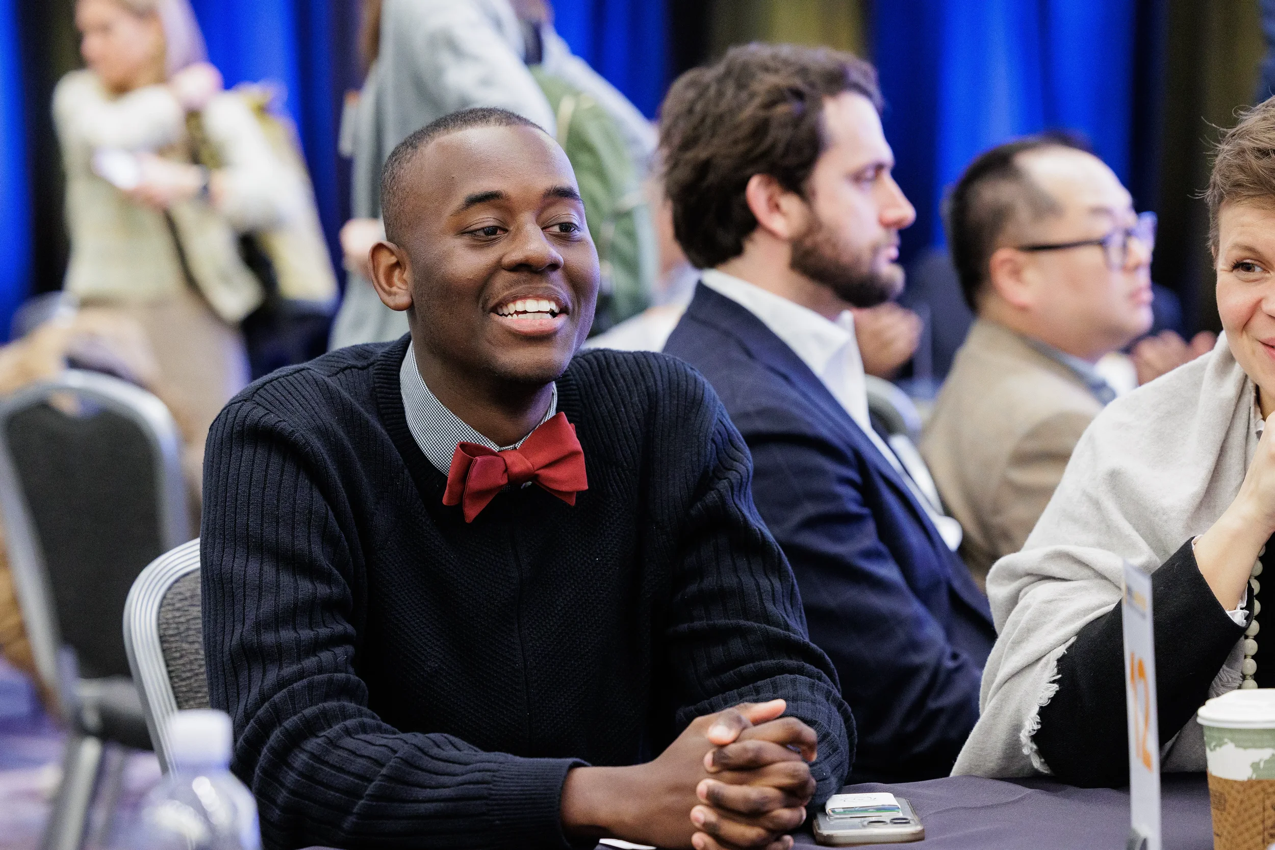 Smiling badged attendee in red bow tie seated at table during Chicago industry corporate conference