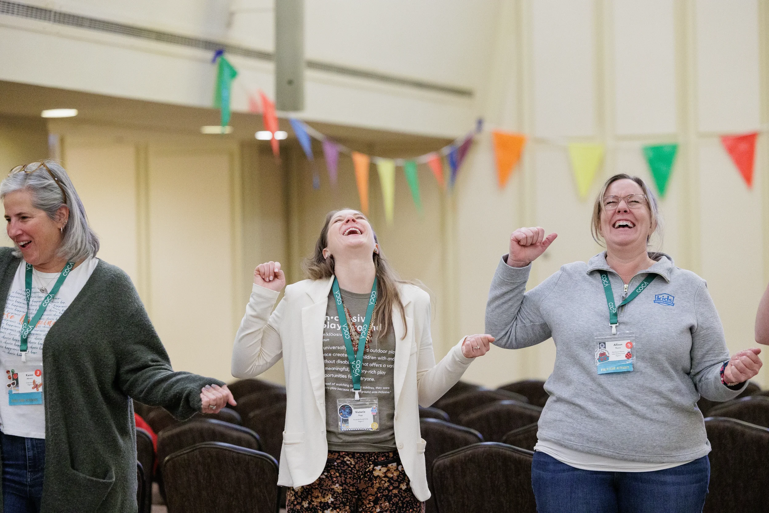 Three attendees wearing conference lanyards laugh together with fists raised during energetic group activity at Orlando nonprofit conference