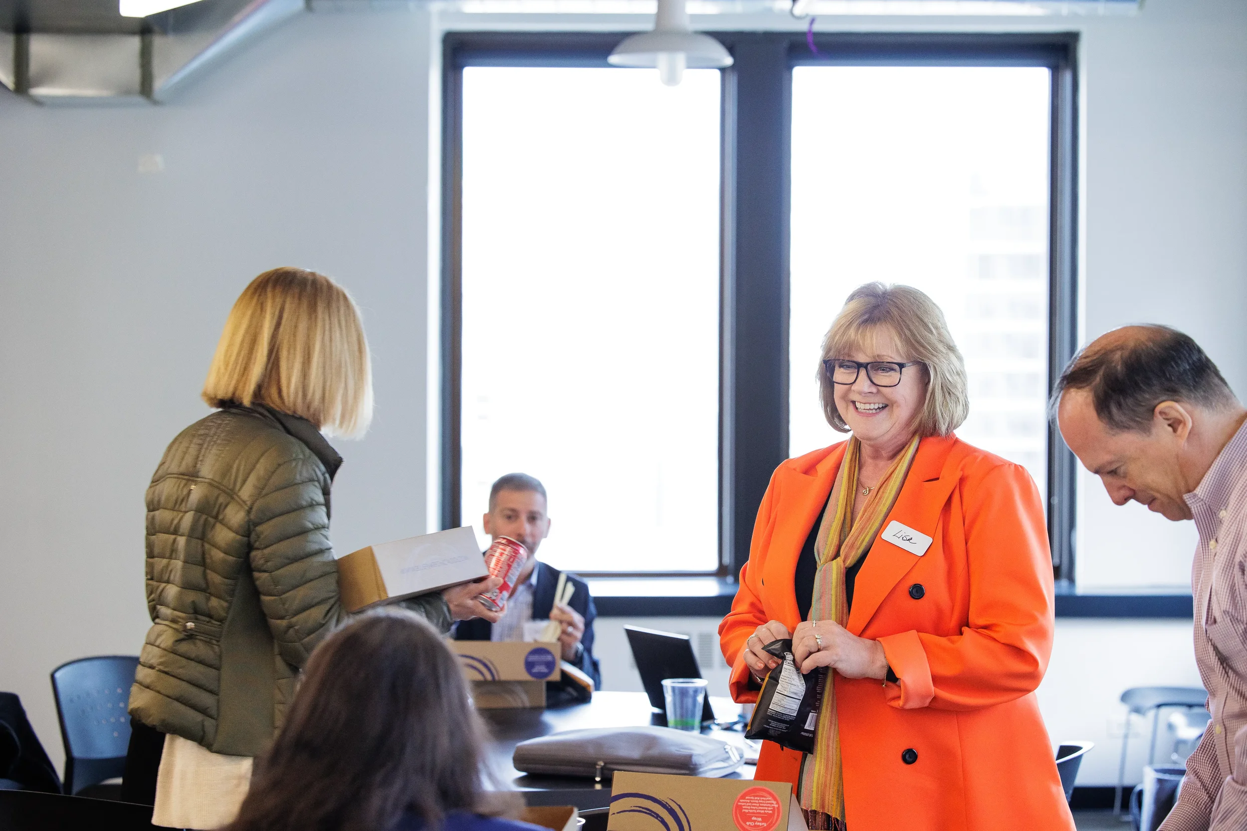 Female attendee in bright orange jacket smiles warmly during a lunch break at Orlando industry conference