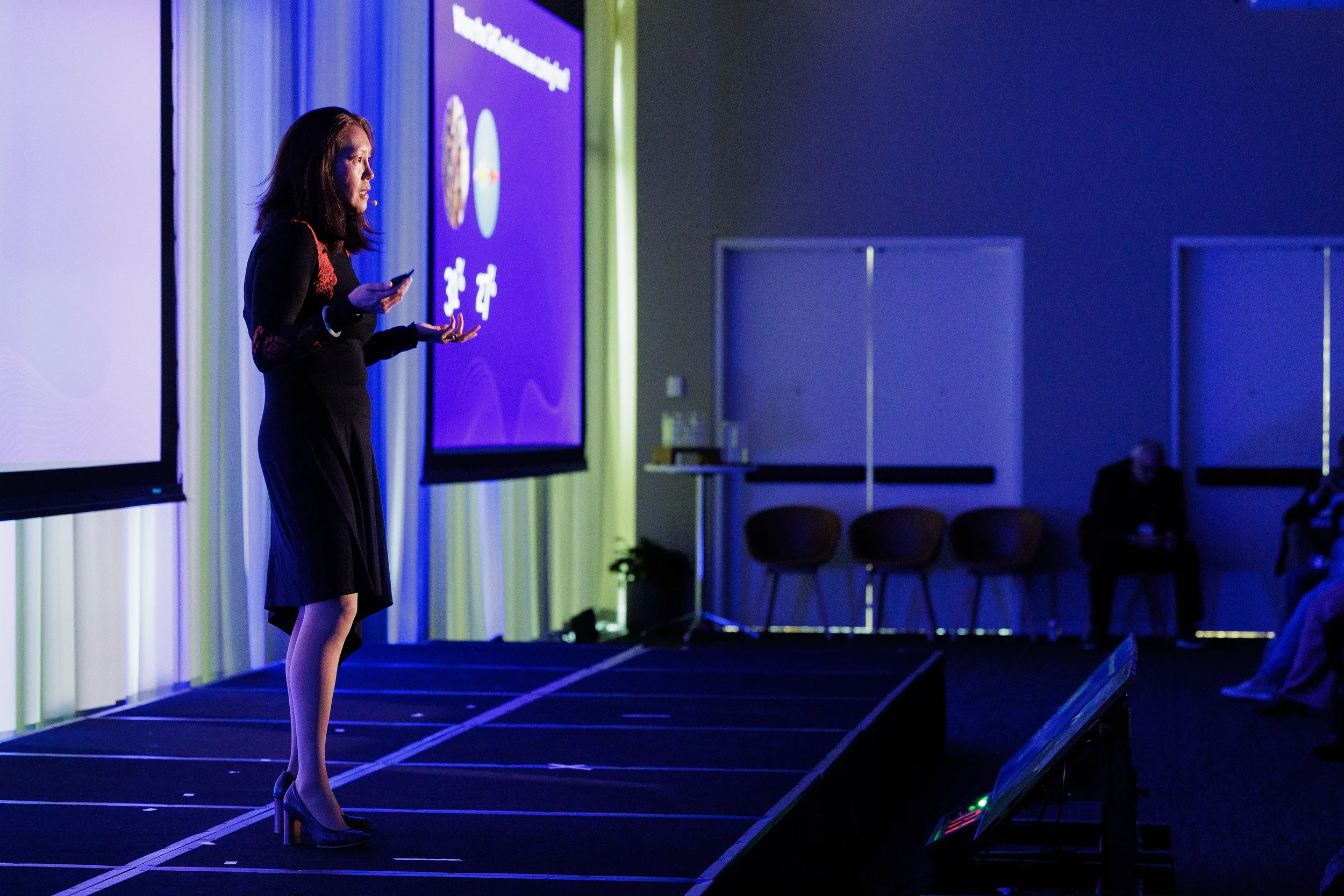 Speaker gestures on stage beside purple presentation slide at Chicago industry conference