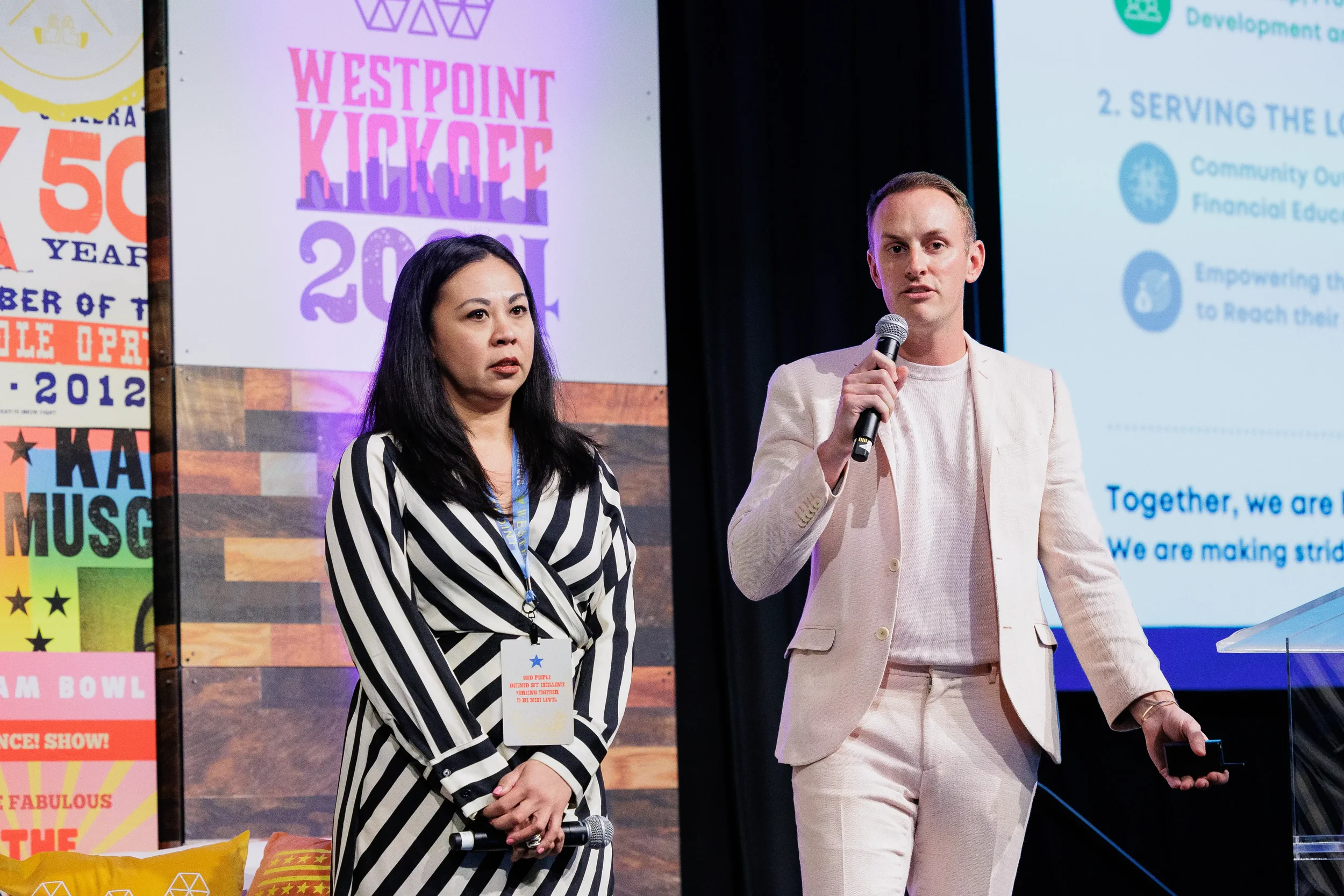 Two presenters stand on stage with microphone in front of branded event backdrop at Chicago corporate conference