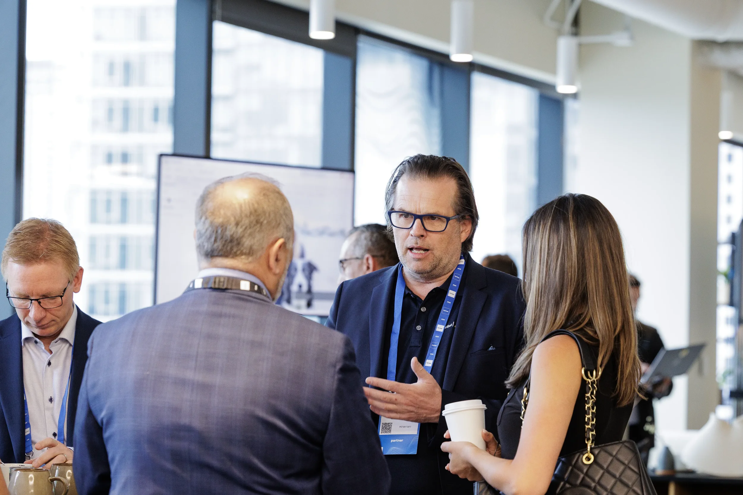 Attendee gestures while talking with colleagues holding coffee in window lounge at Orlando corporate event