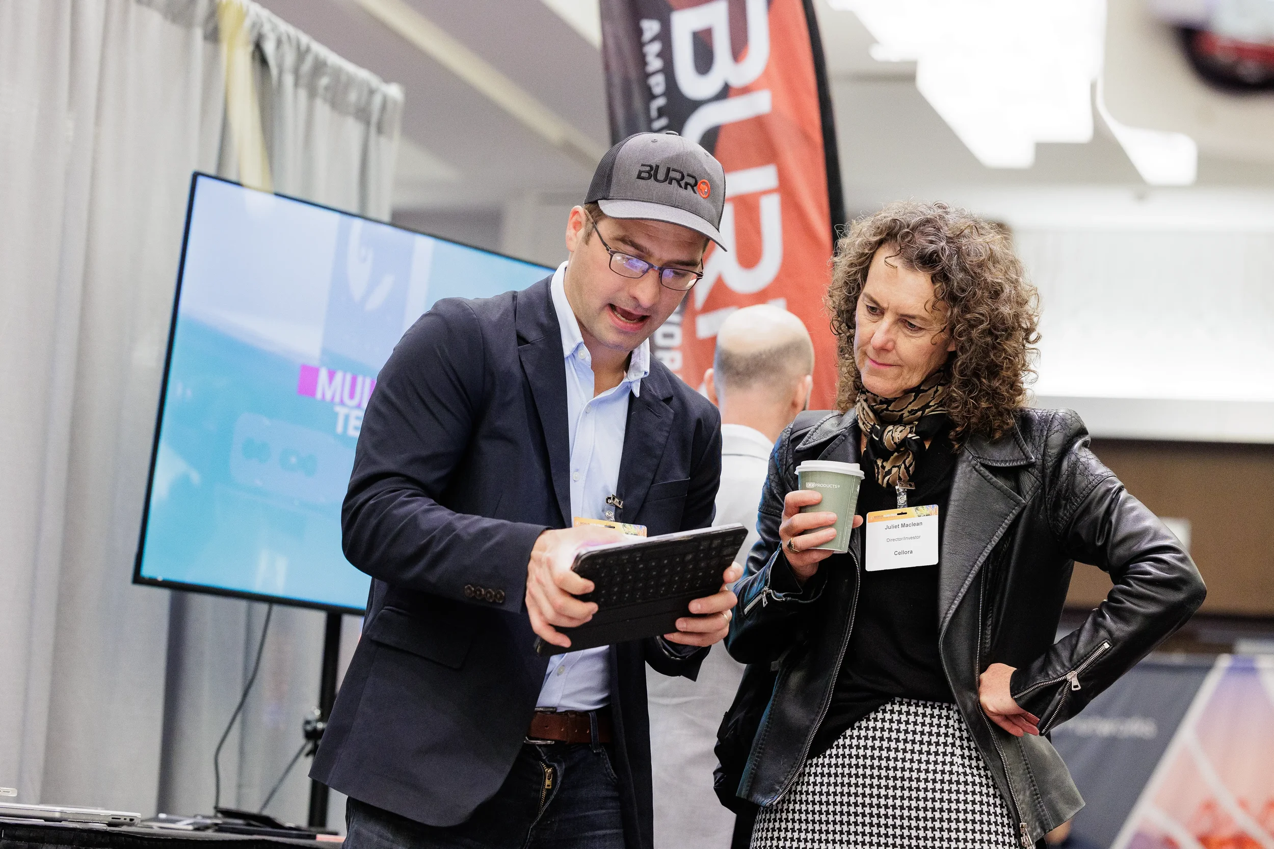 Exhibitor with name badge demonstrates tablet to attendee at trade show booth at Chicago industry conference