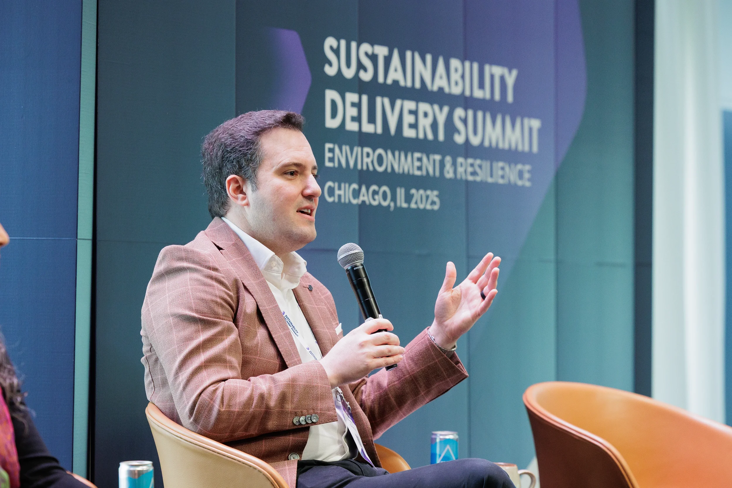 Panelist gestures while speaking with microphone on branded stage at Chicago industry summit