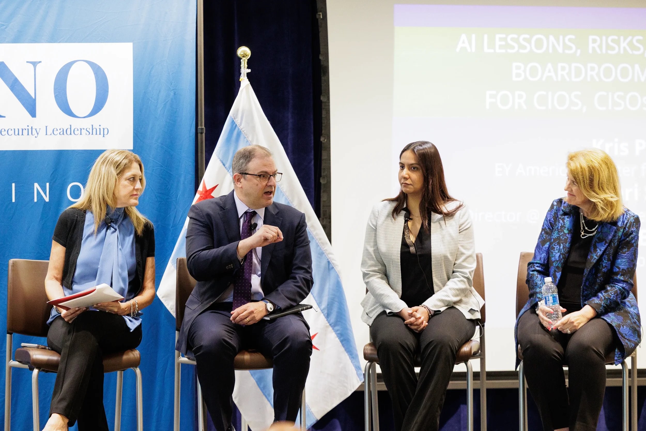 Four panelists seated on stage beside Chicago flag during industry panel discussion at Chicago corporate conference