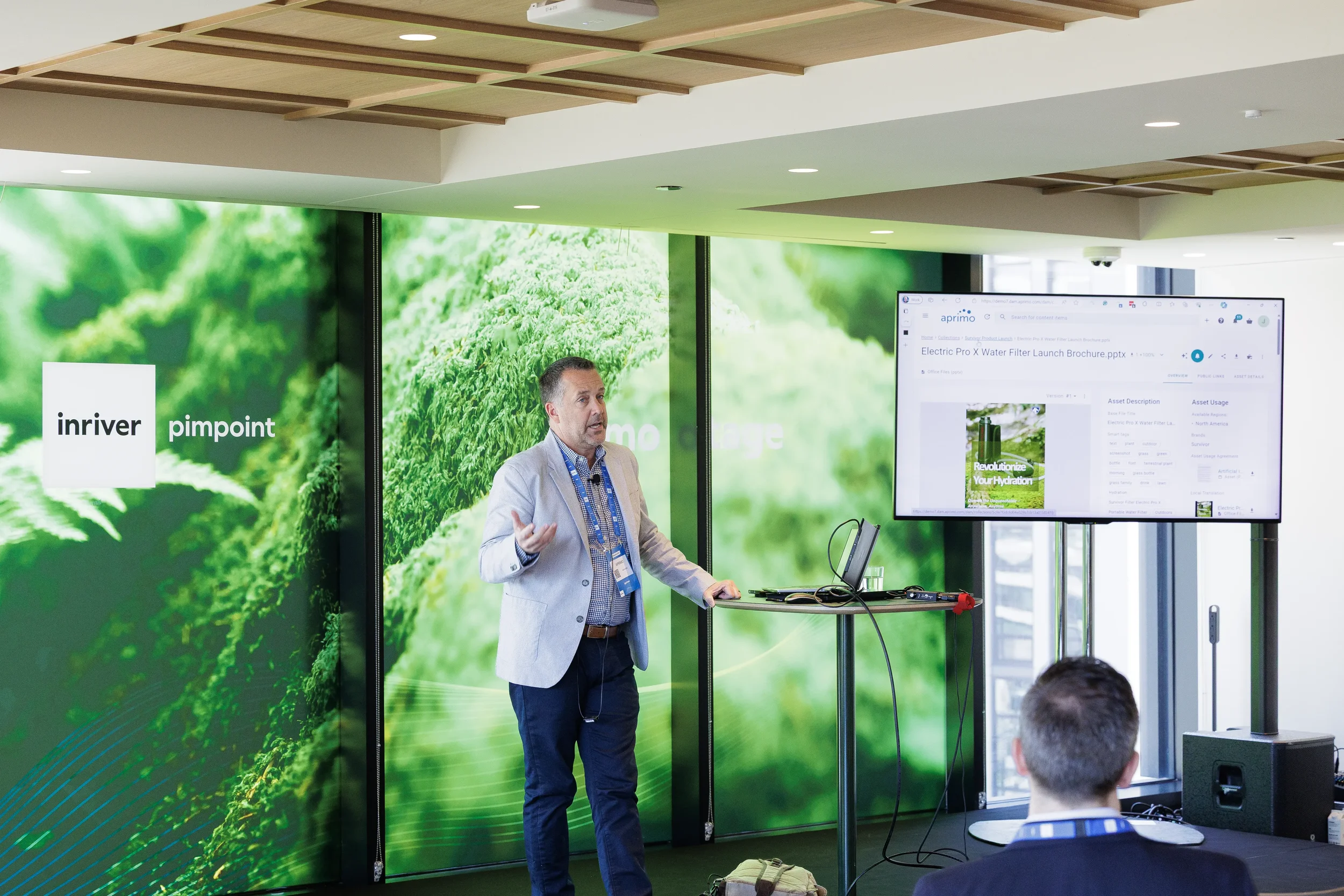 Presenter gestures beside software demo screen on breakout stage at Orlando industry conference