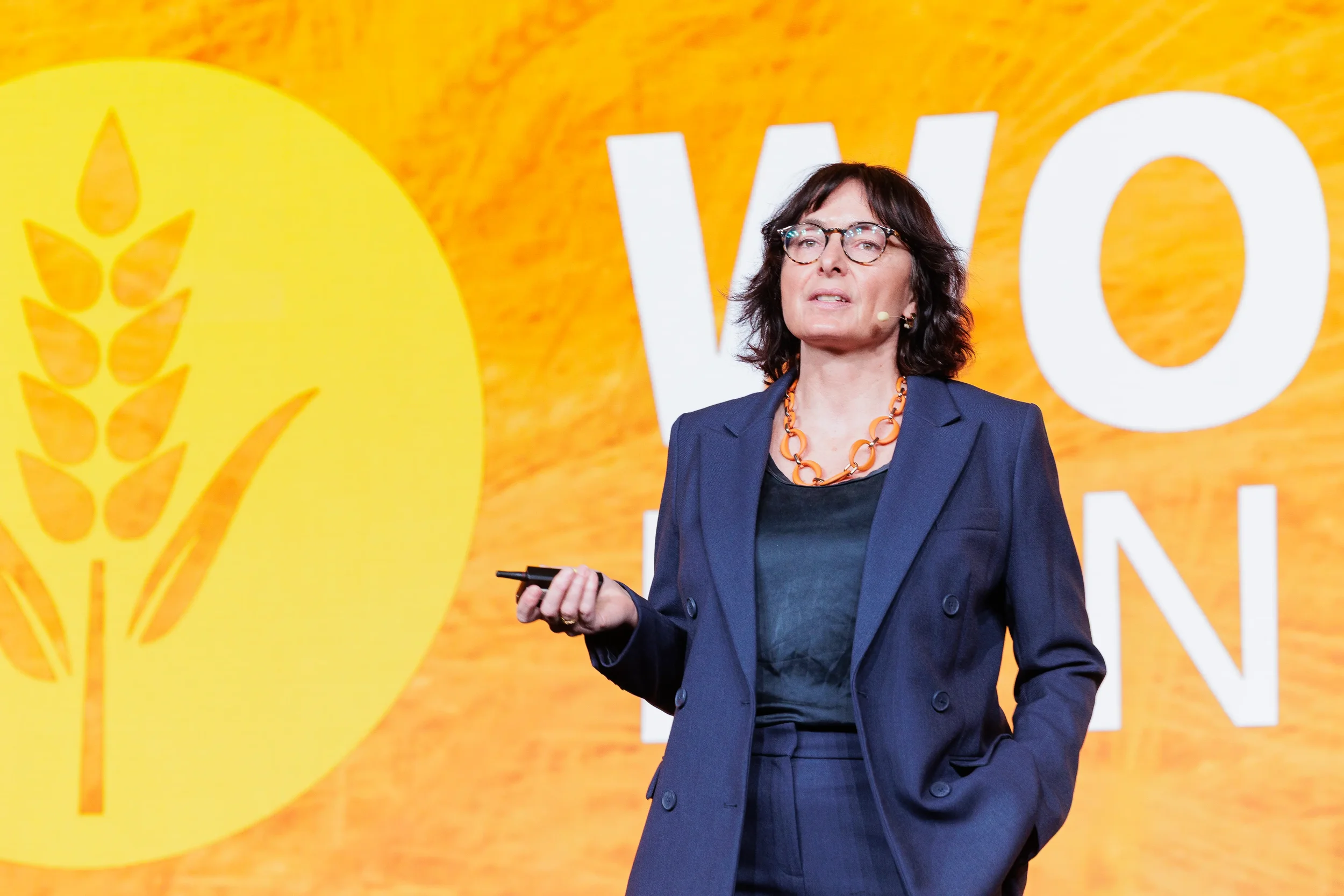Female keynote speaker in navy blazer with orange necklace presents on stage at Chicago corporate event