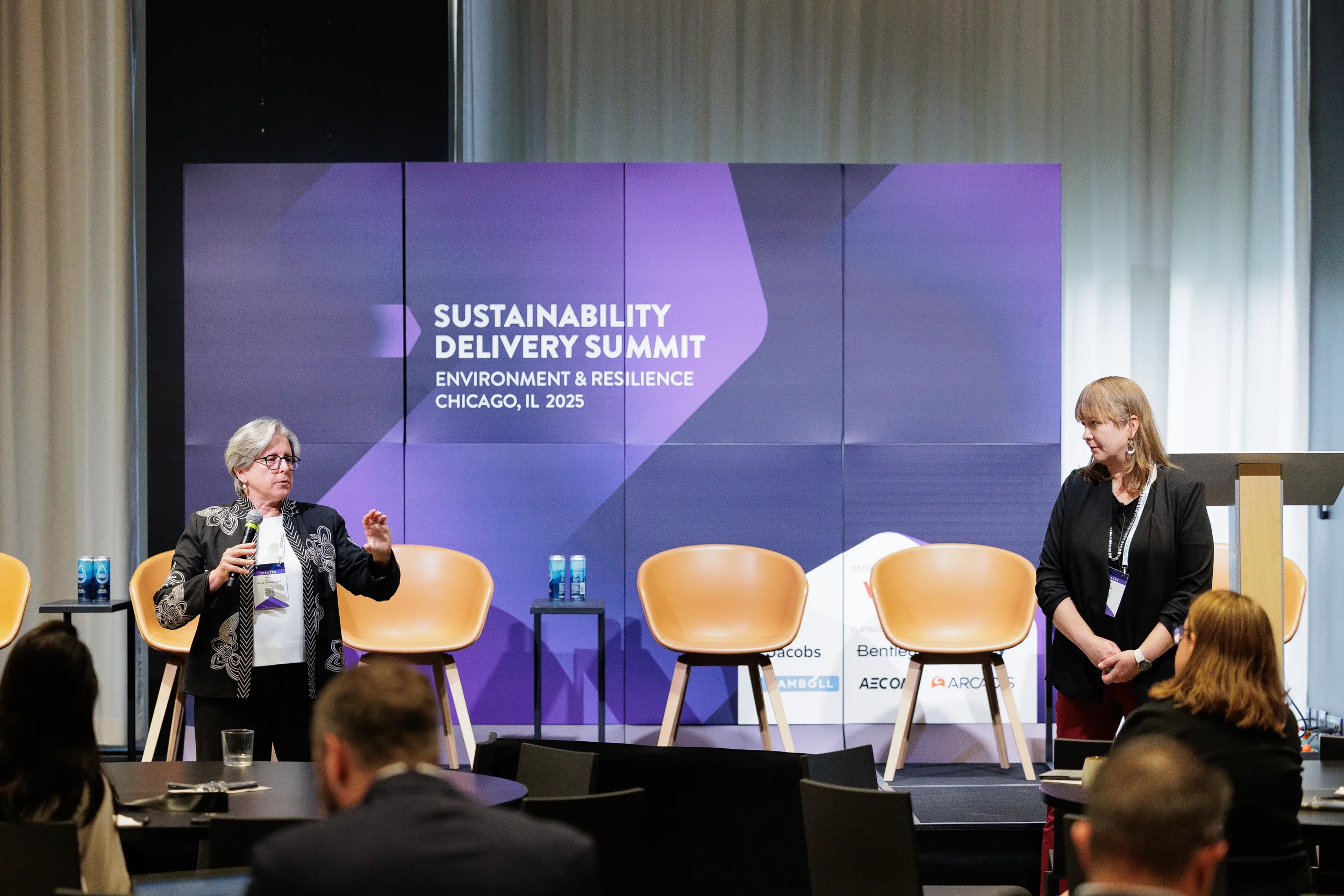Two panelists gesture while speaking on branded stage at Chicago industry conference