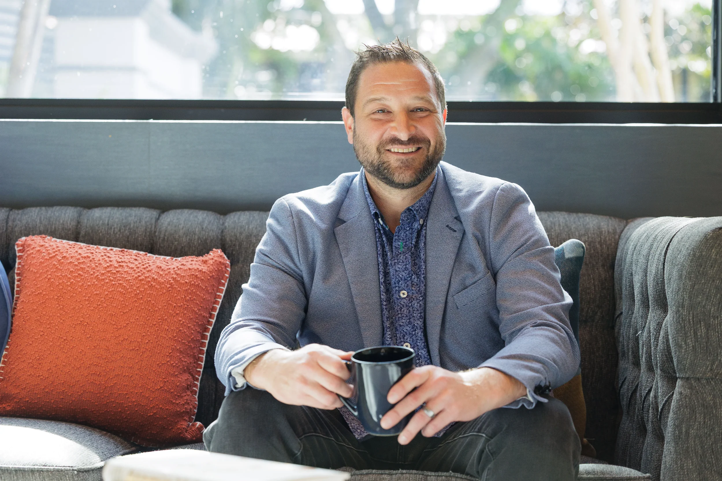 Smiling male attendee holds coffee mug while relaxing on hotel lounge sofa at Orlando corporate event