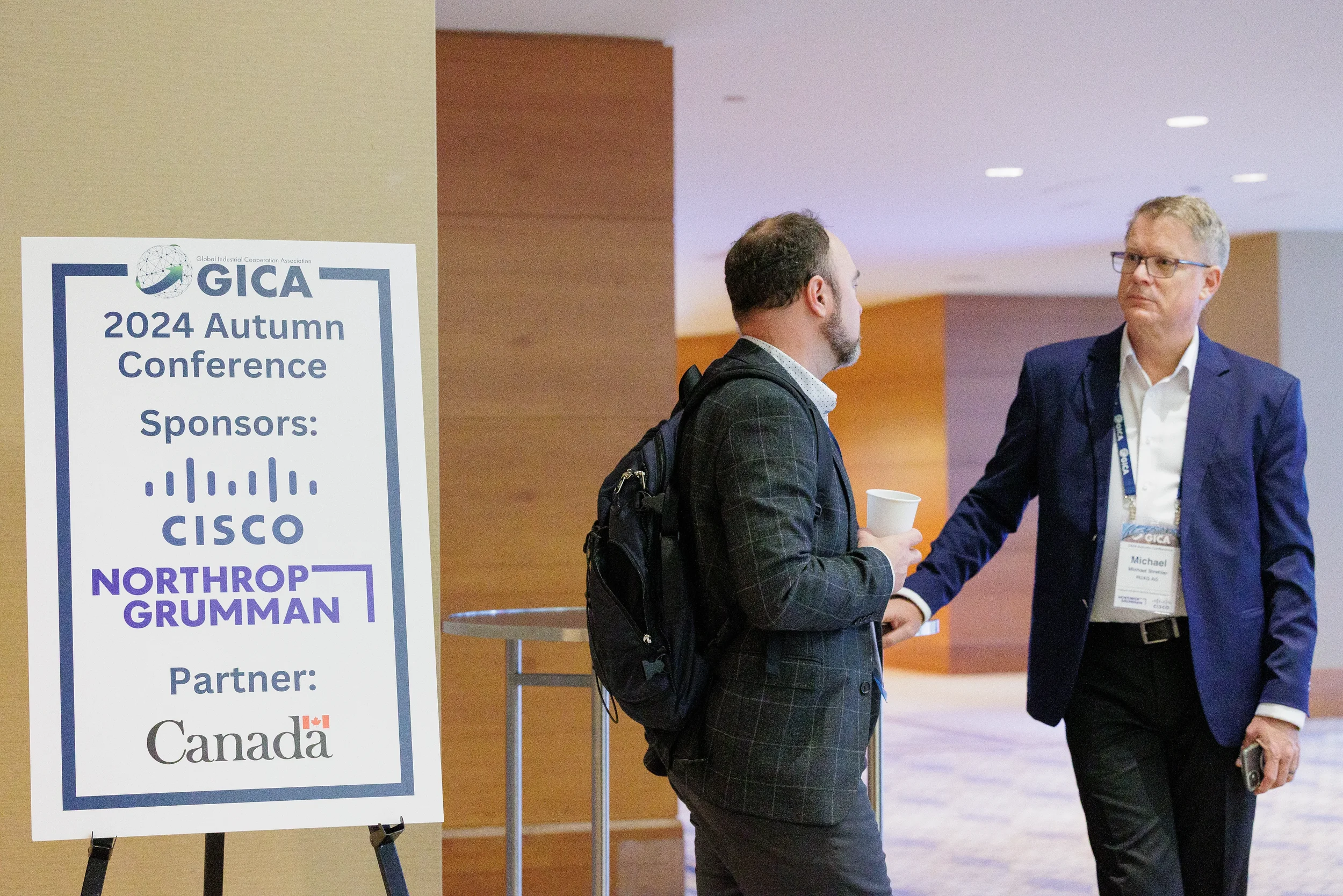 Two conference attendees greet each other in hotel lobby near sponsor signage at Chicago corporate event