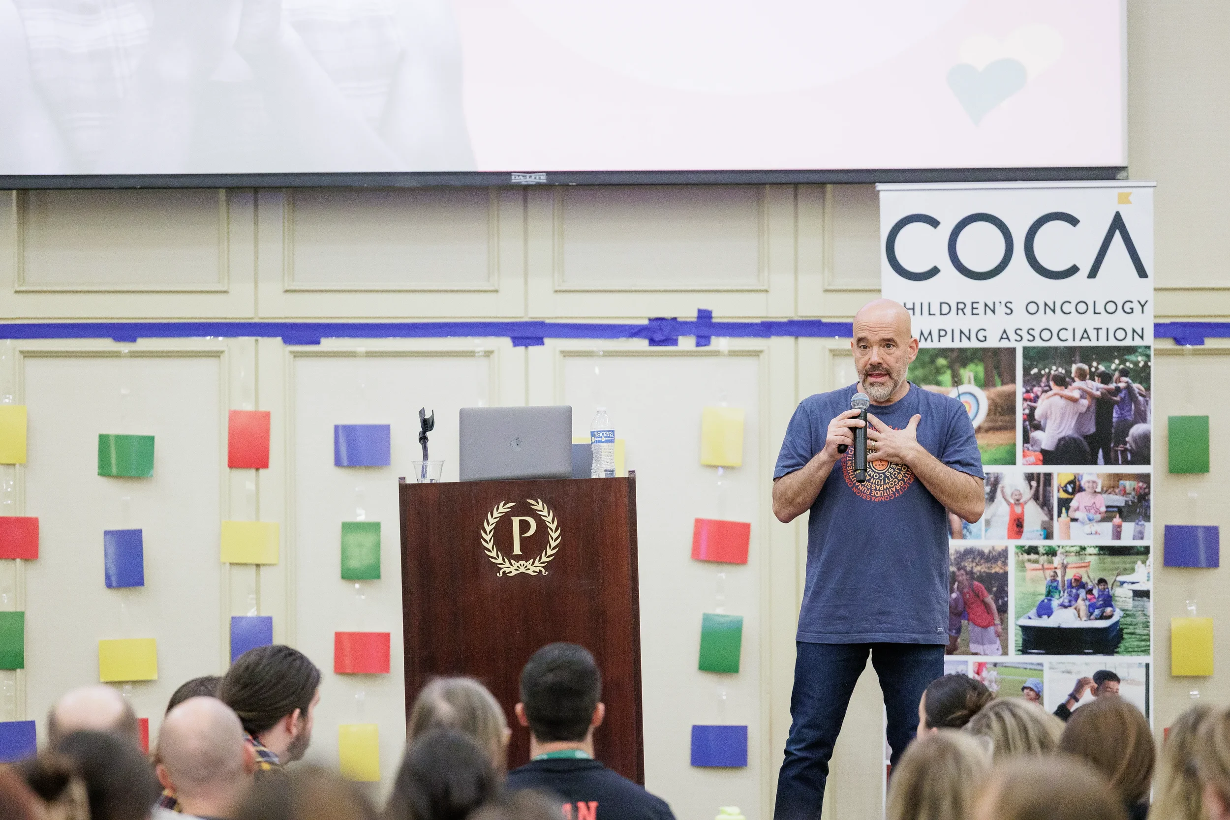 Keynote speaker holds microphone and addresses audience in front of branded backdrop at Orlando nonprofit conference