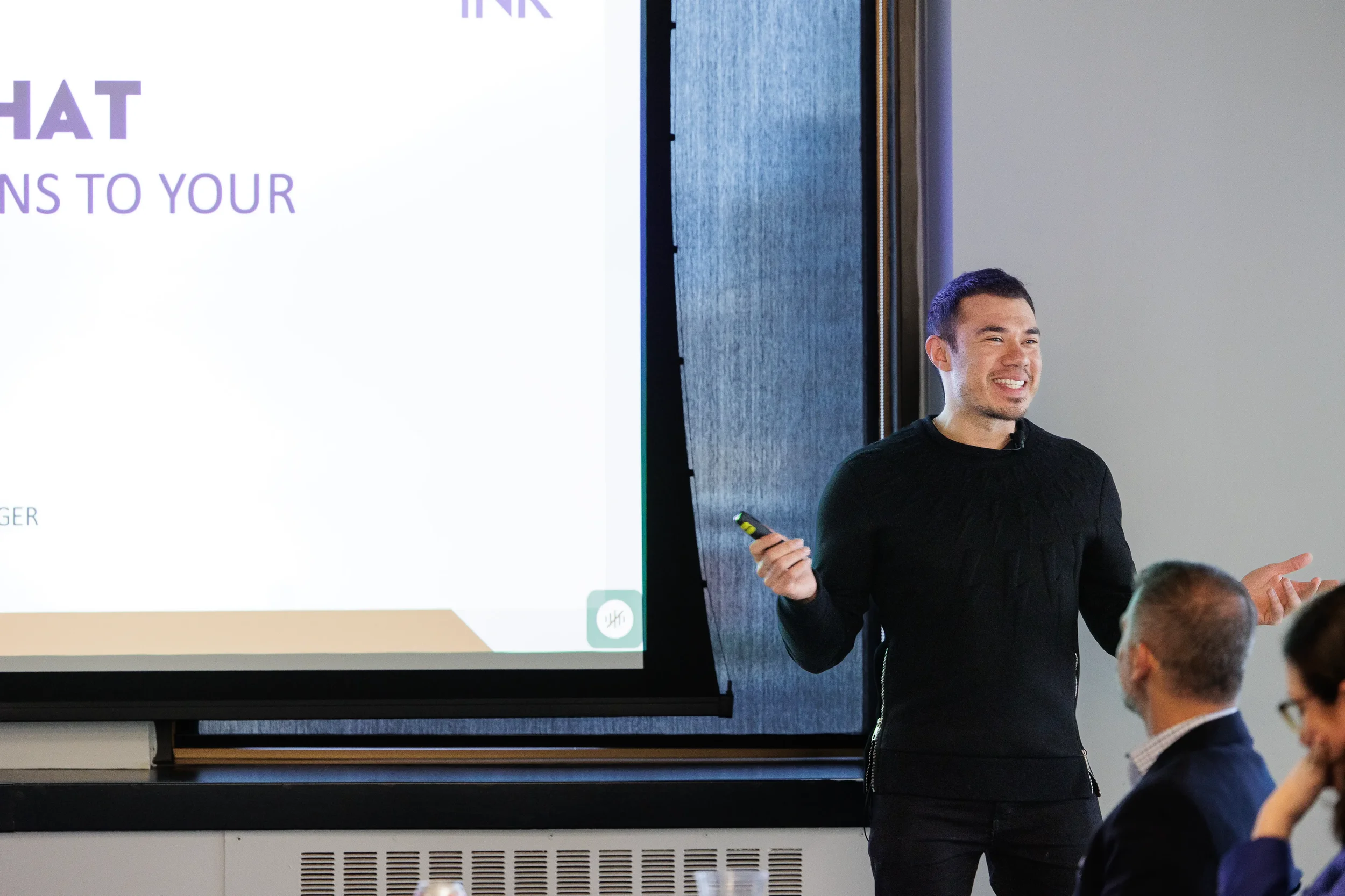 Male speaker smiles while presenting beside large projection screen at Orlando industry conference
