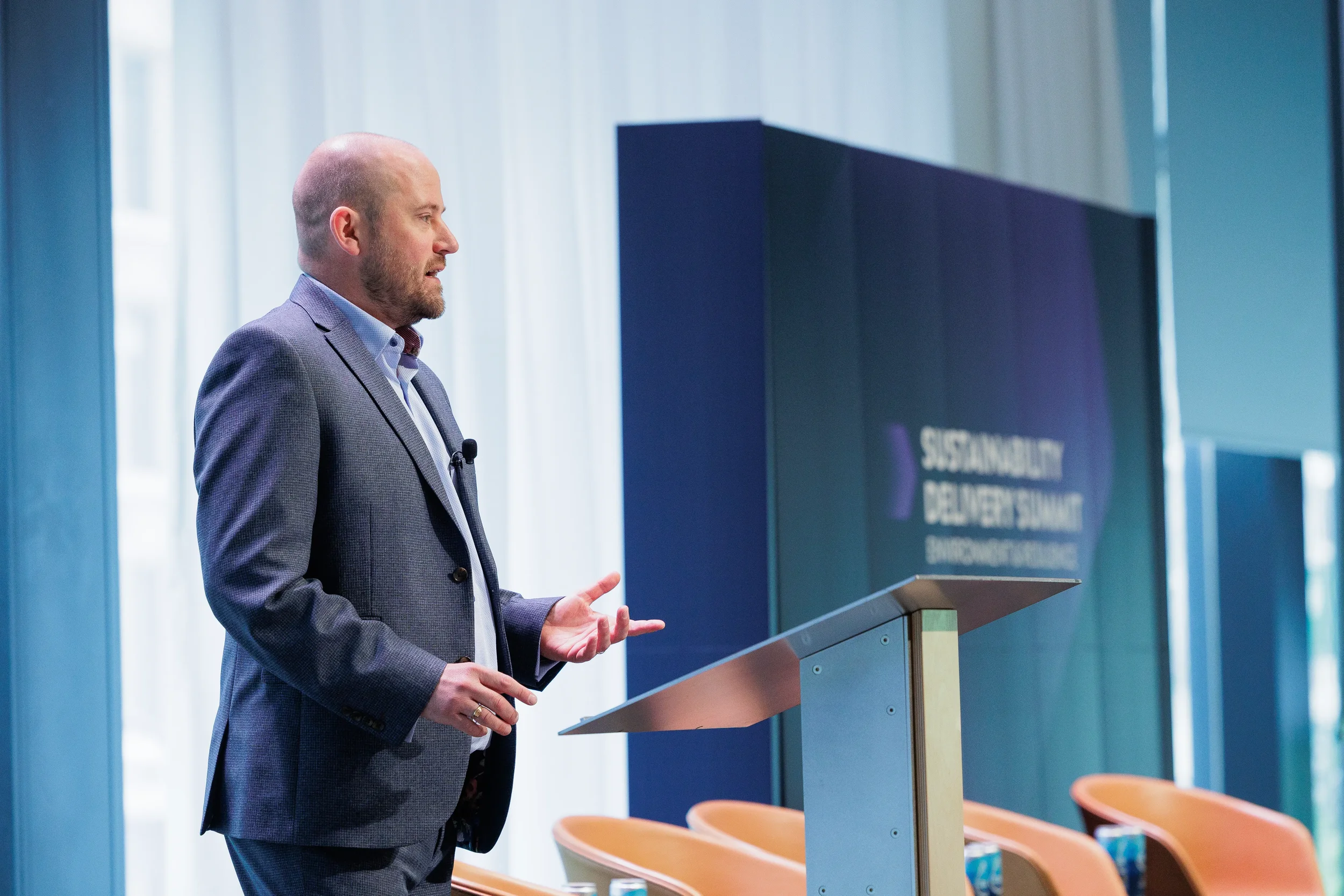 Speaker gestures while presenting from podium in profile view at Orlando industry conference