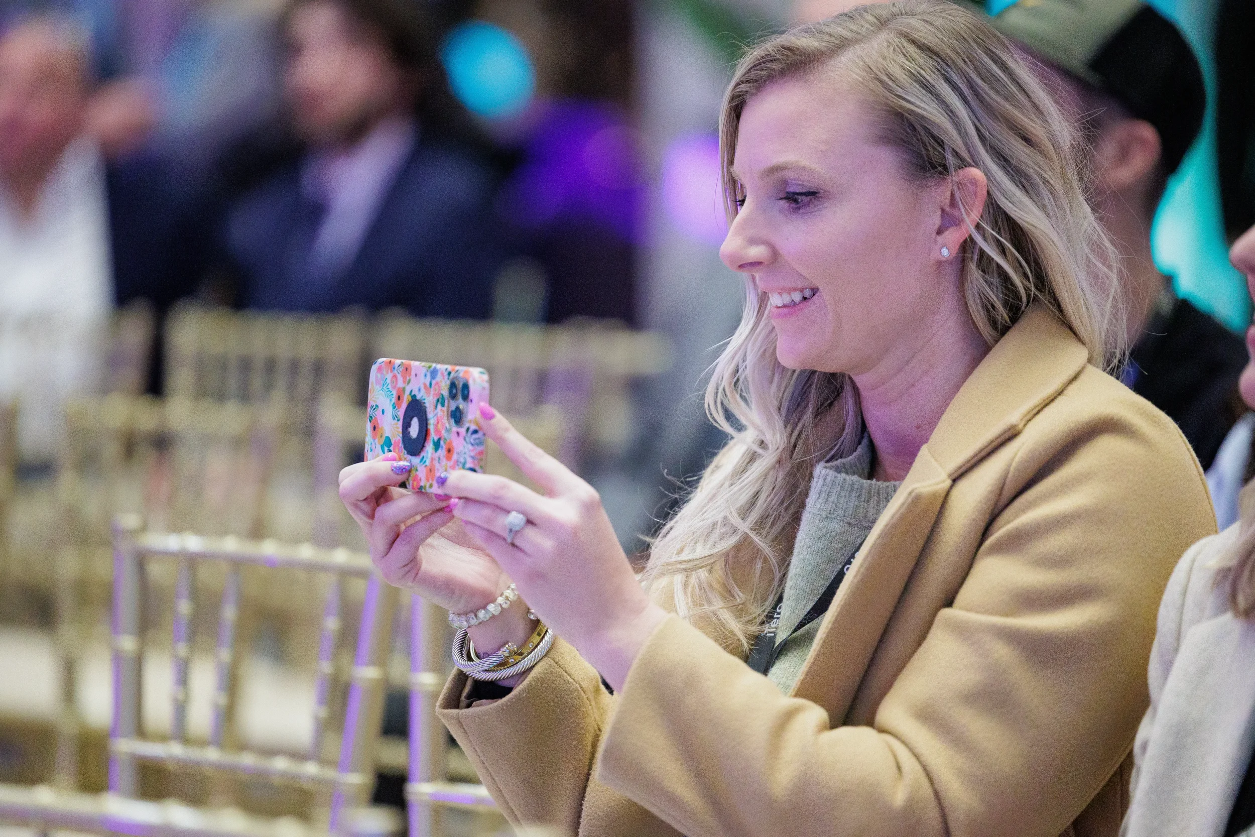 Smiling attendee holds up phone to photograph stage during session at Orlando corporate event