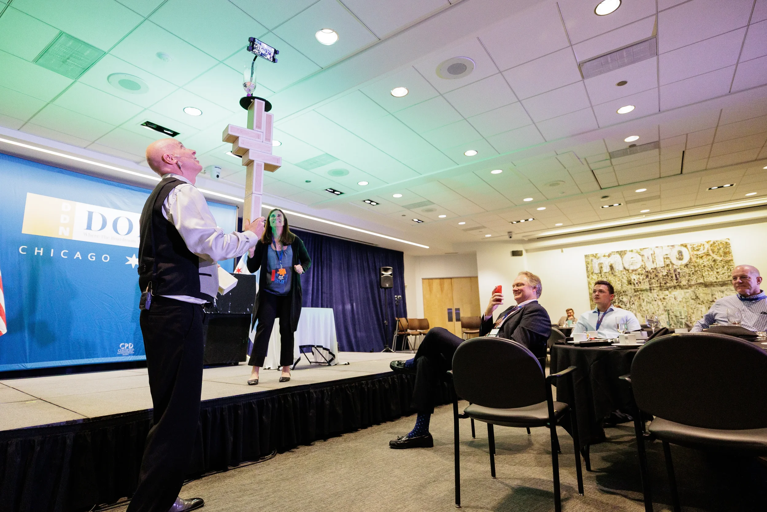 Entertainer balances tall object on chin before amused audience at Chicago corporate conference event