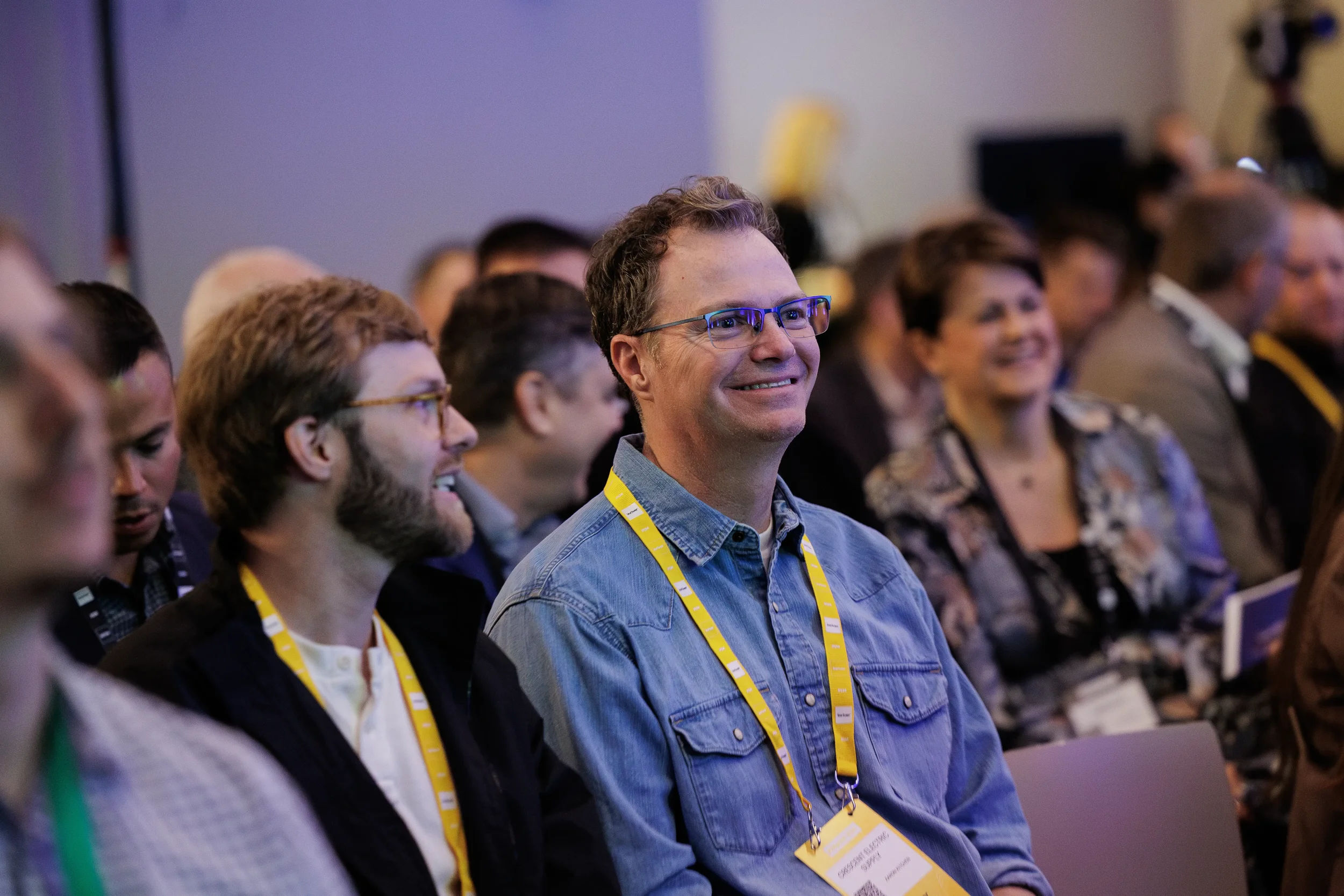 Smiling attendee in denim shirt with yellow lanyard enjoys session at Chicago corporate conference