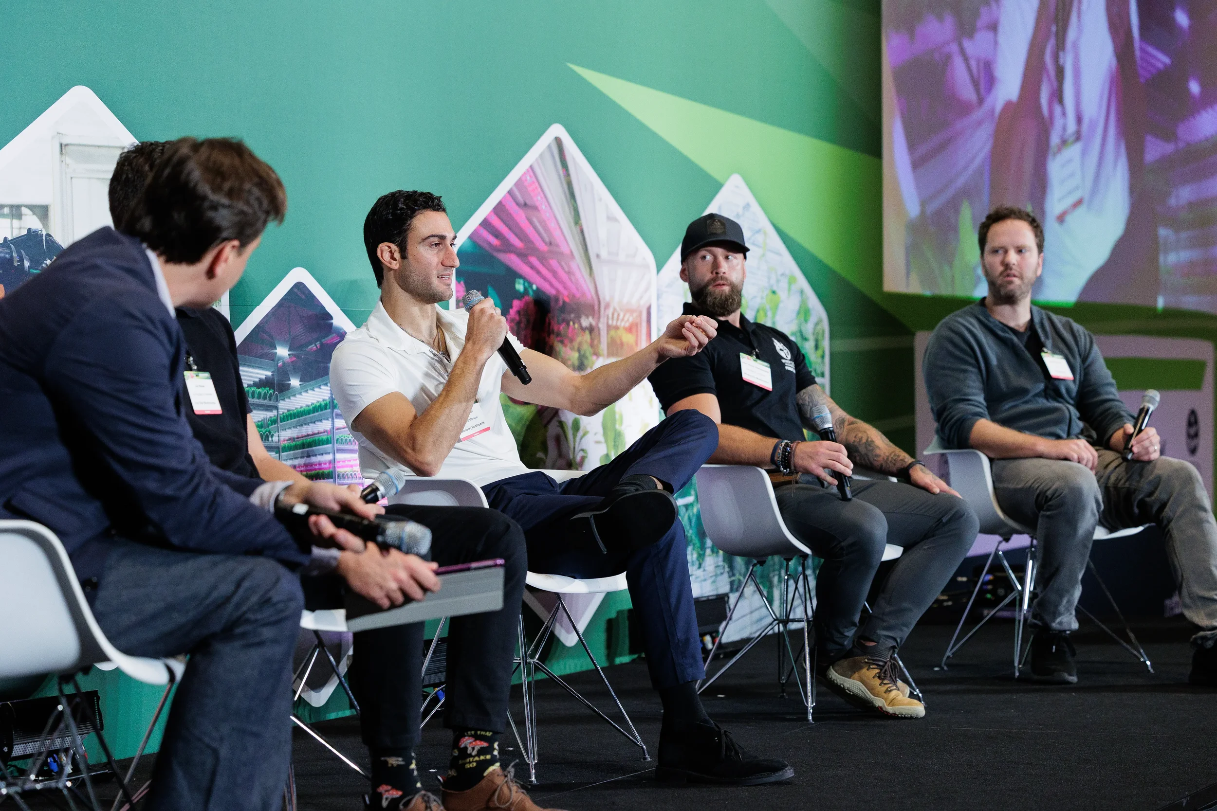 Panelist speaks into microphone while fellow speakers listen on stage in front of green branded backdrop at Chicago industry conference