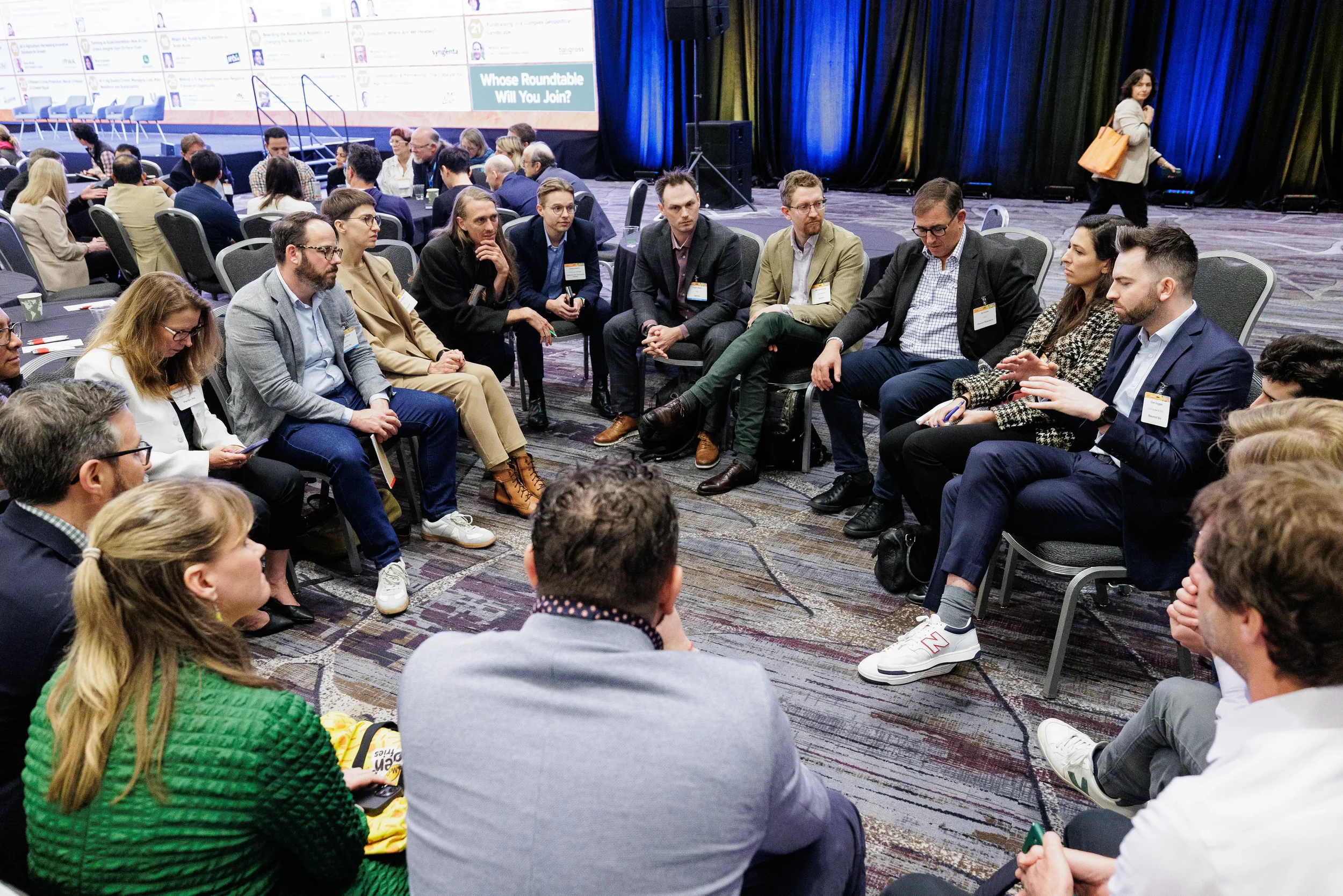 Large group of badged attendees seated in circle for roundtable discussion at Chicago industry conference