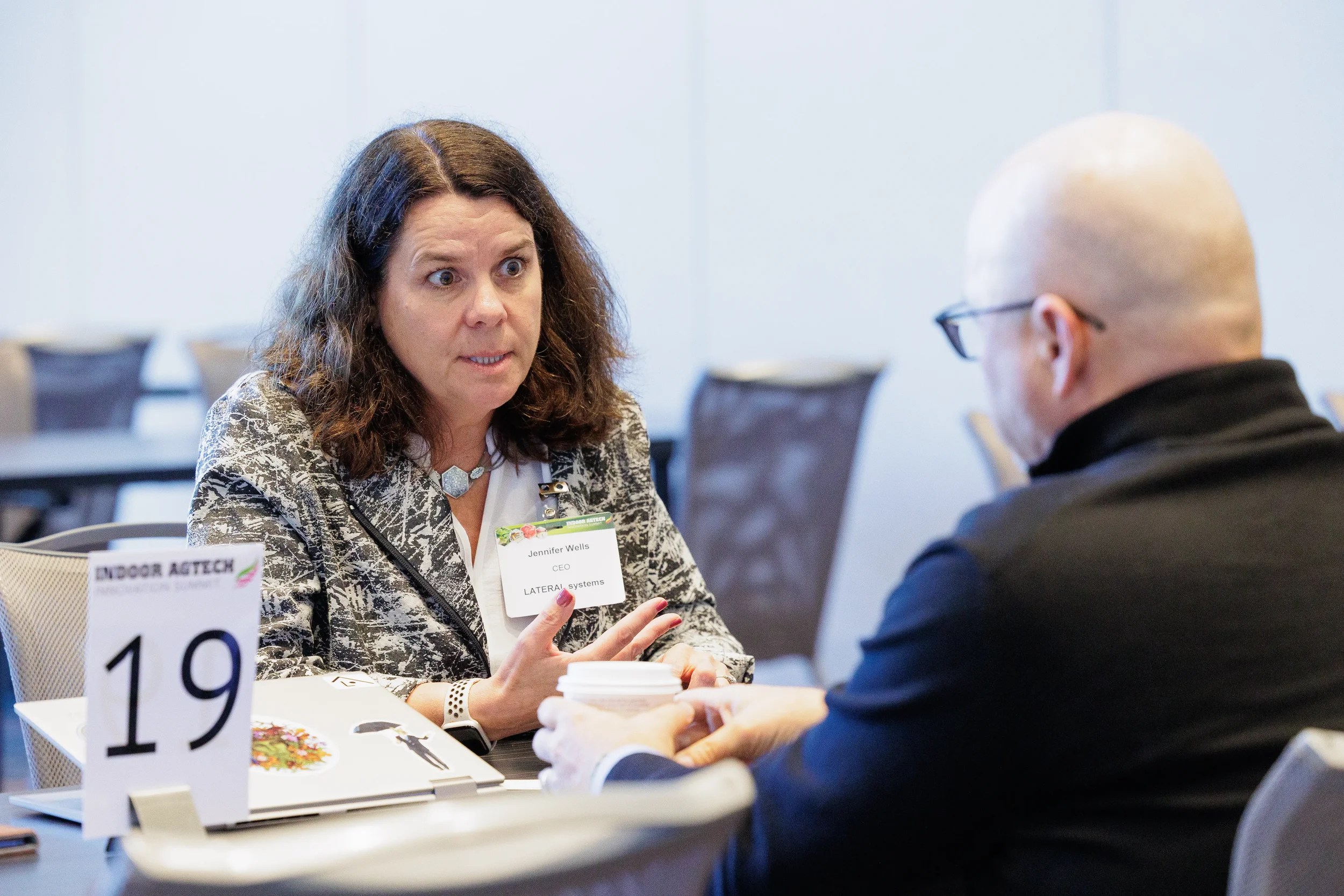 Attendee gestures while speaking with fellow attendee at numbered table during Orlando industry conference