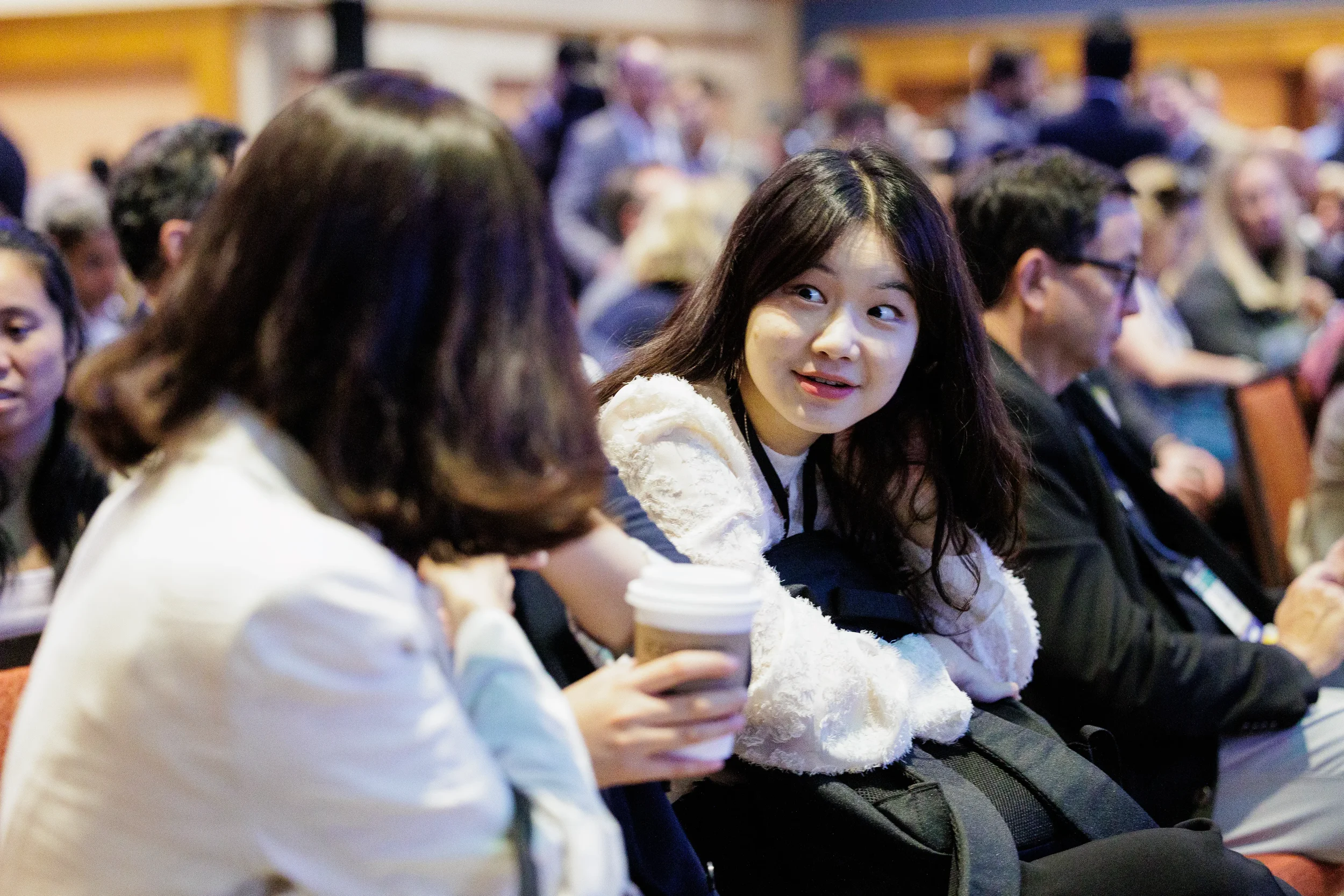 Attendee smiles while holding coffee during seated session at Orlando industry conference