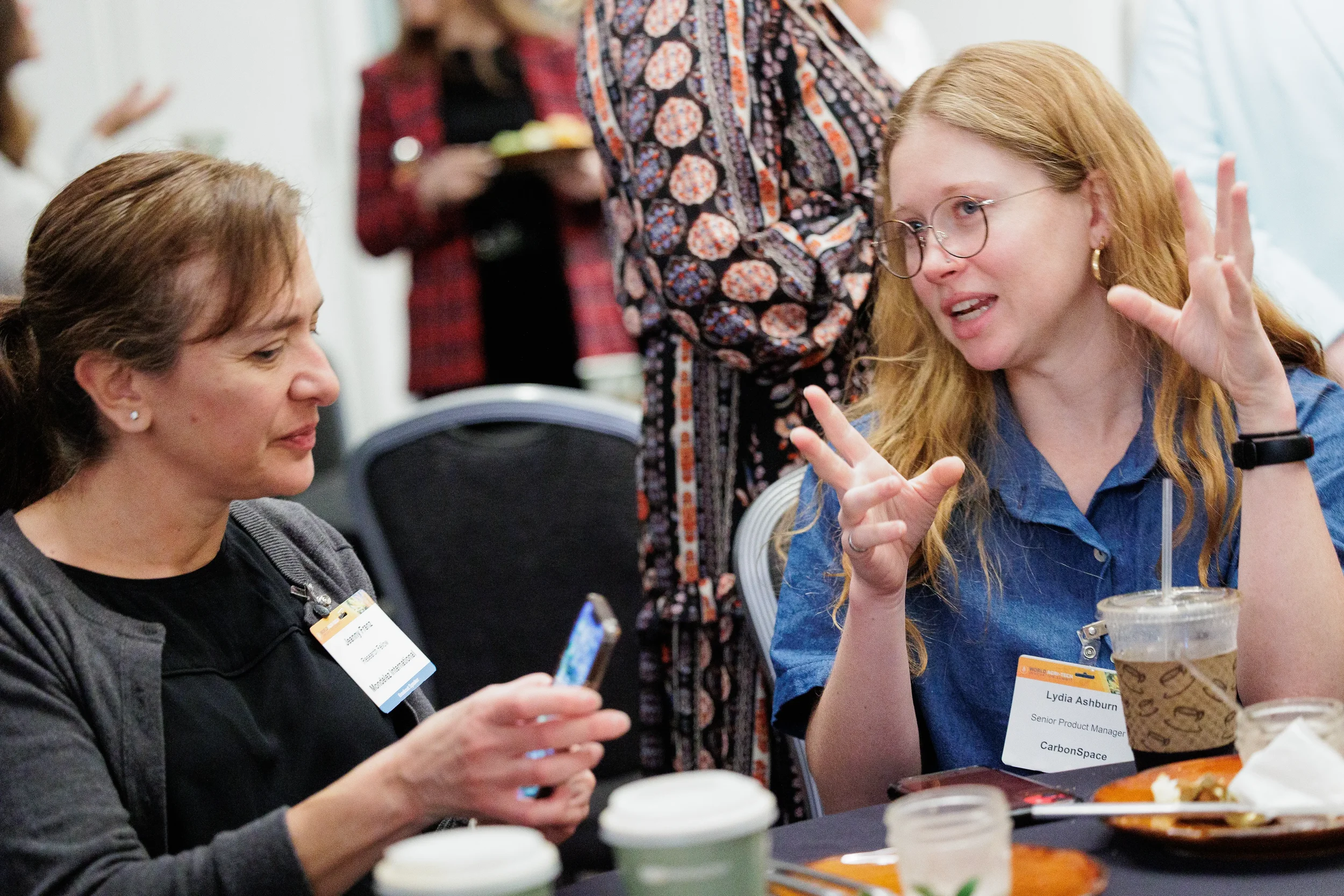 Two attendees with name badges engage in animated conversation at table during Orlando corporate conference