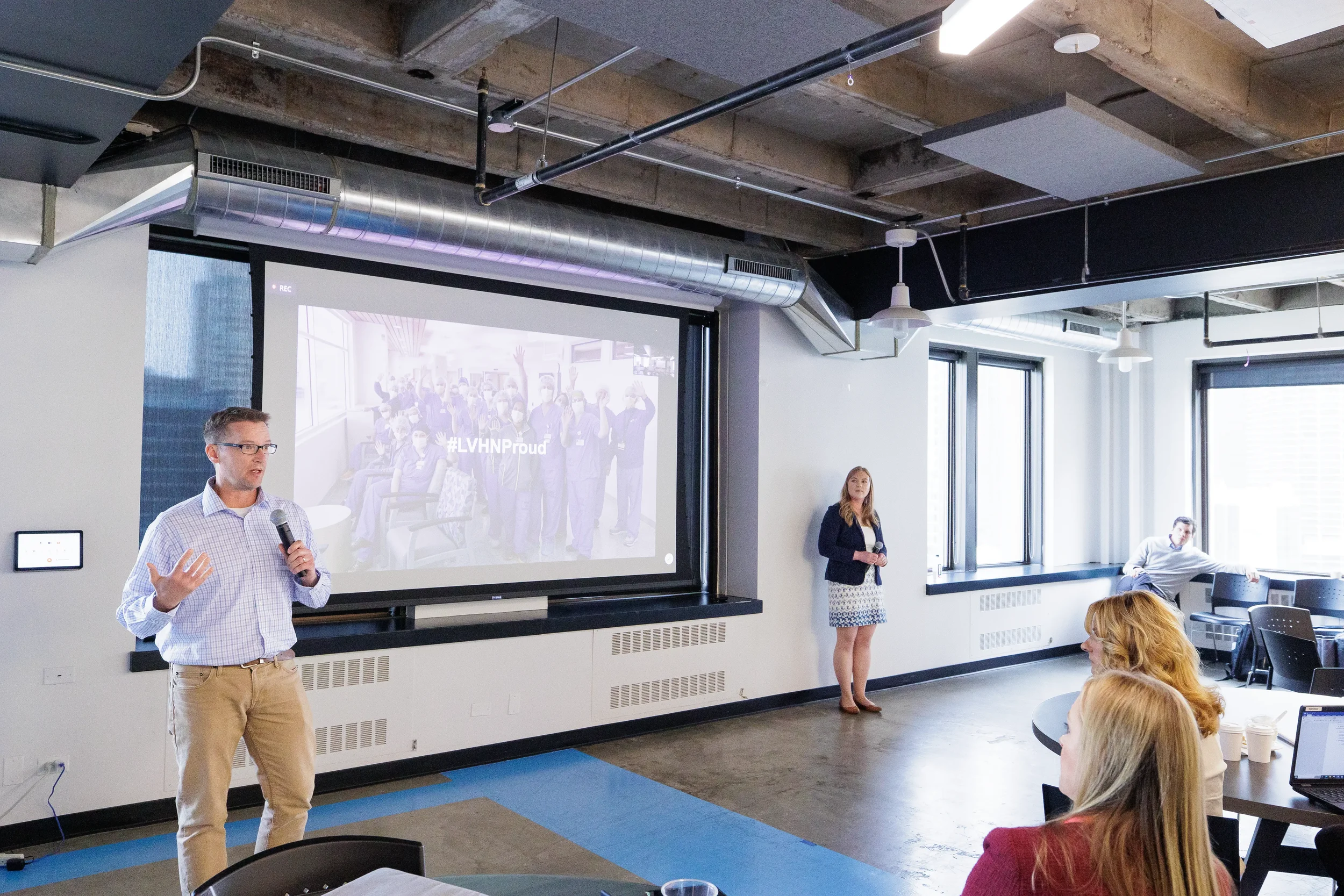 Male speaker presents with microphone beside a large projection screen at Chicago industry conference