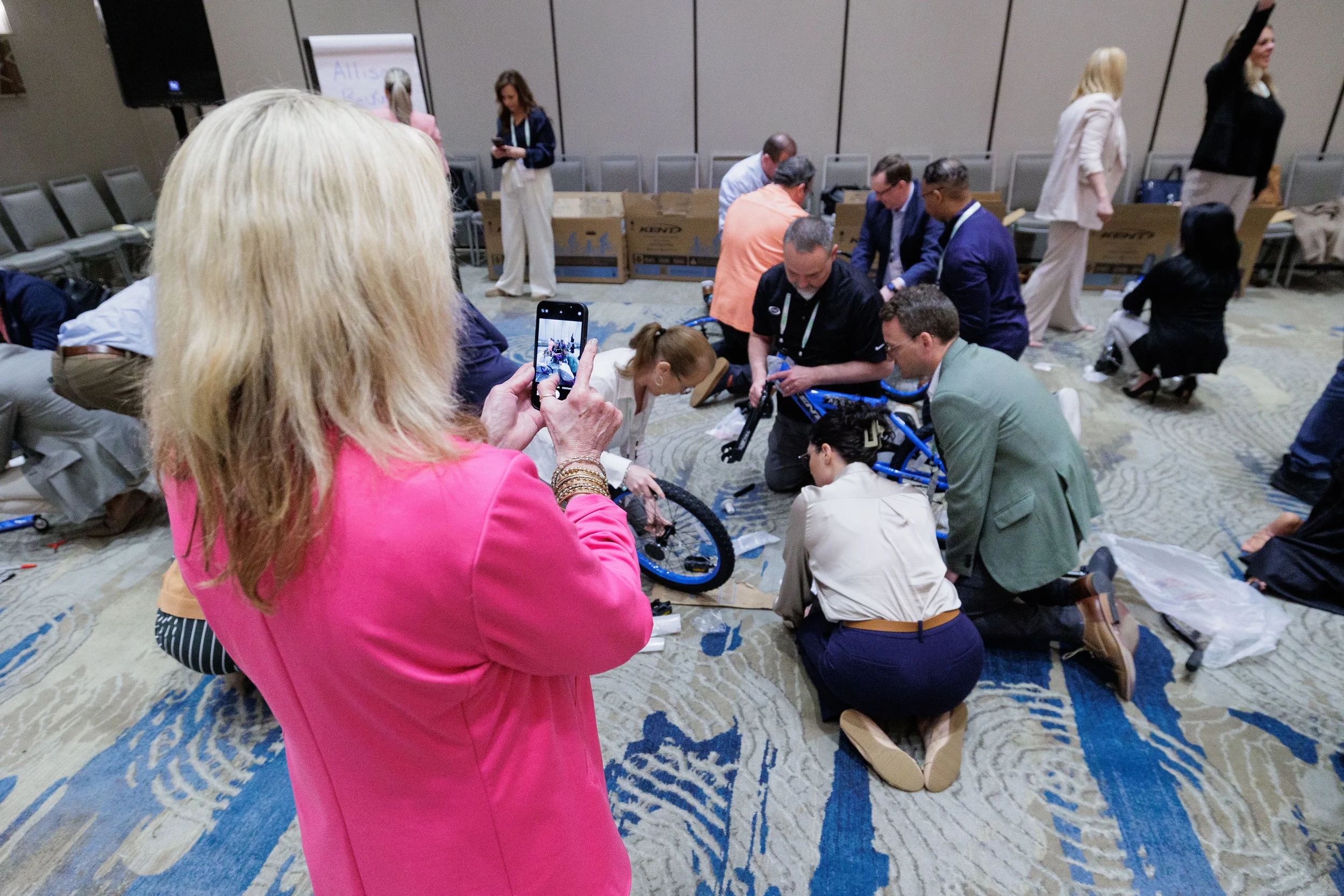 Attendees kneel on ballroom floor assembling blue bicycles during team building at Orlando corporate conference