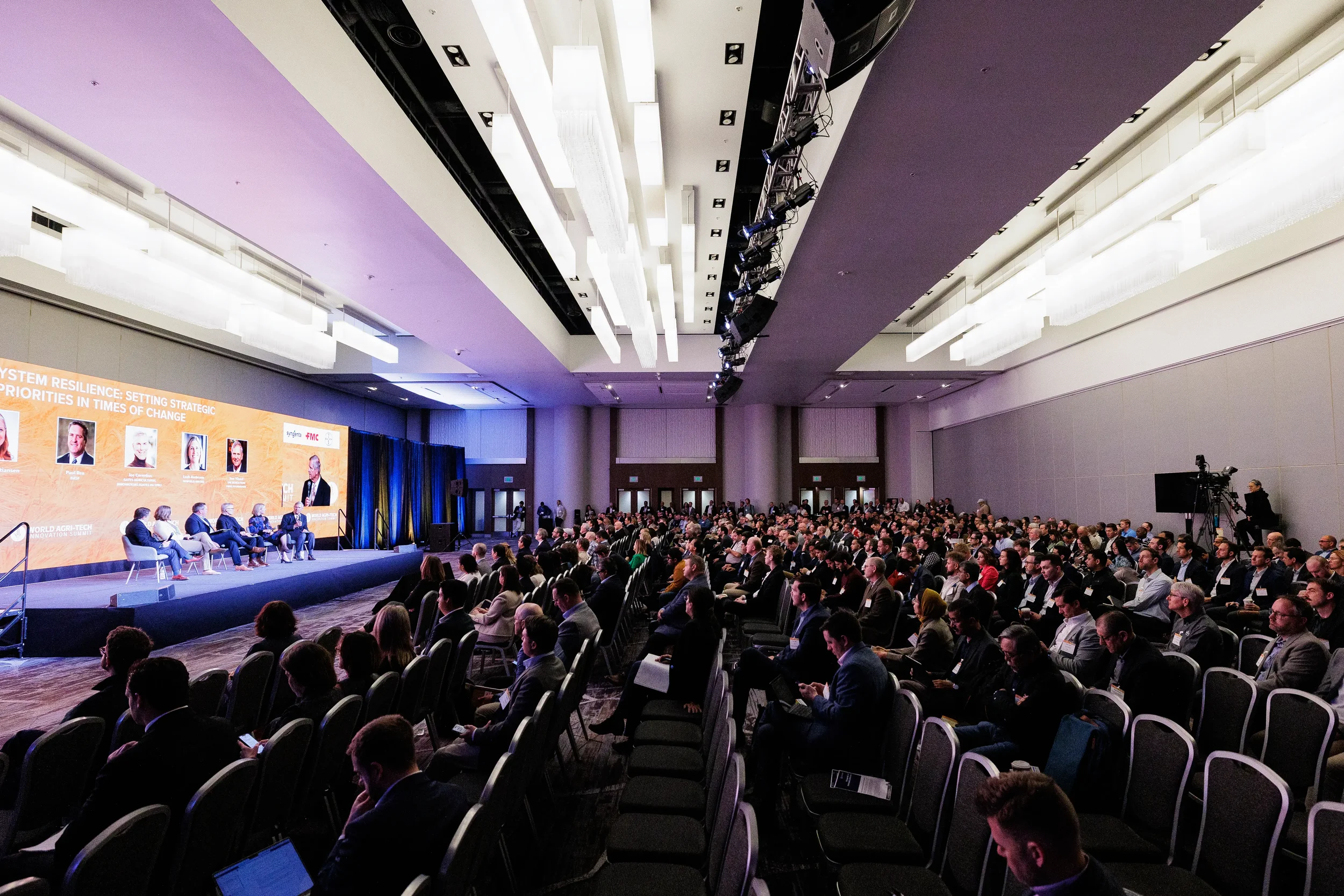 Wide angle of packed ballroom with panel on branded stage at Chicago corporate industry conference