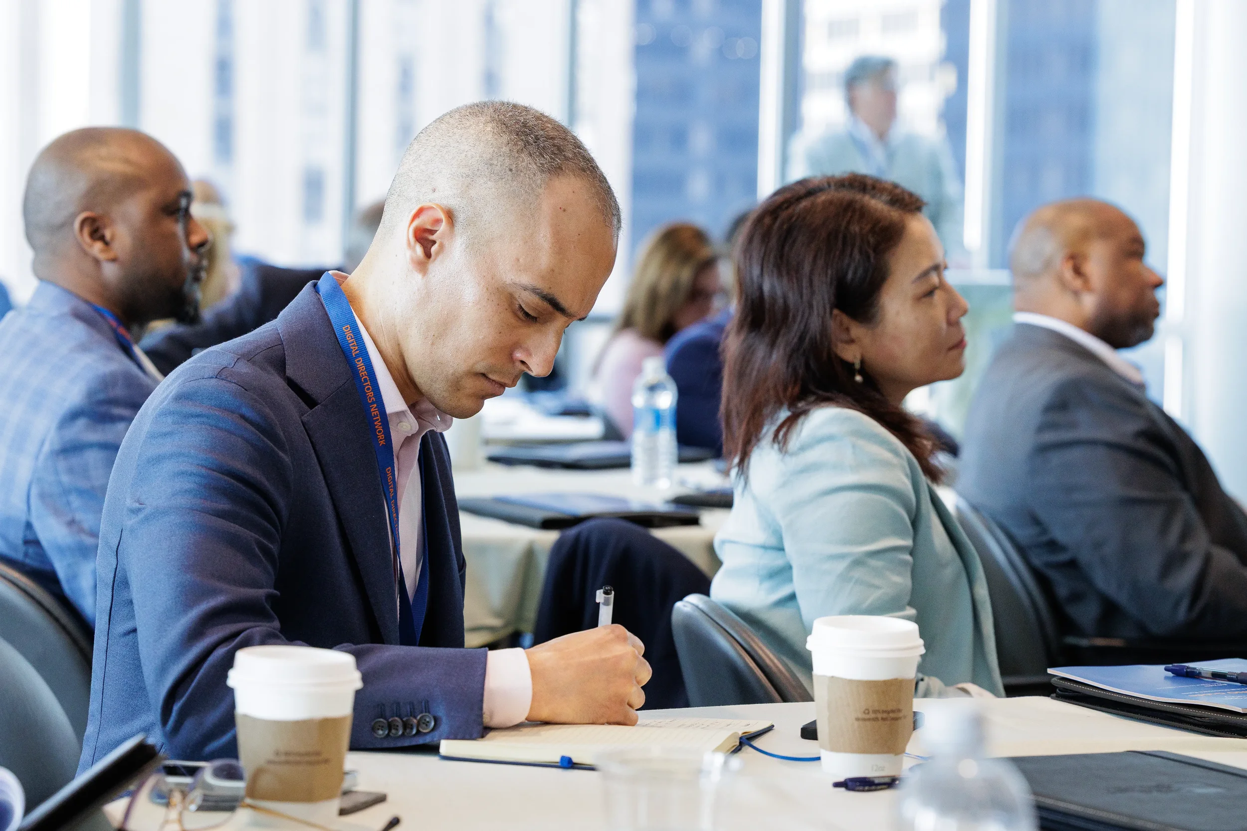 Male attendee with lanyard writes notes beside coffee cup during Orlando industry conference session