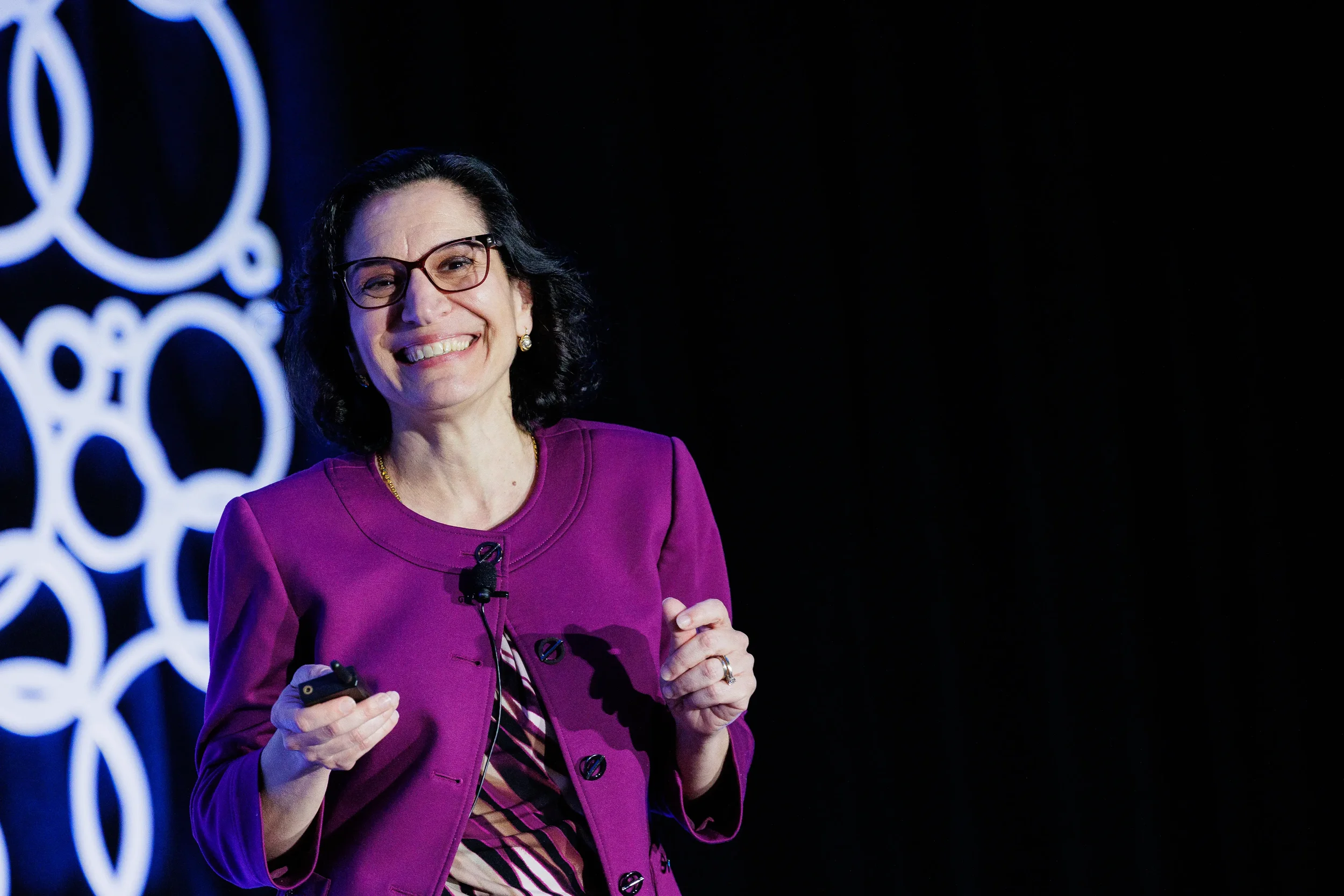 Presenter in magenta jacket laughs while holding slide clicker on stage at Orlando industry conference