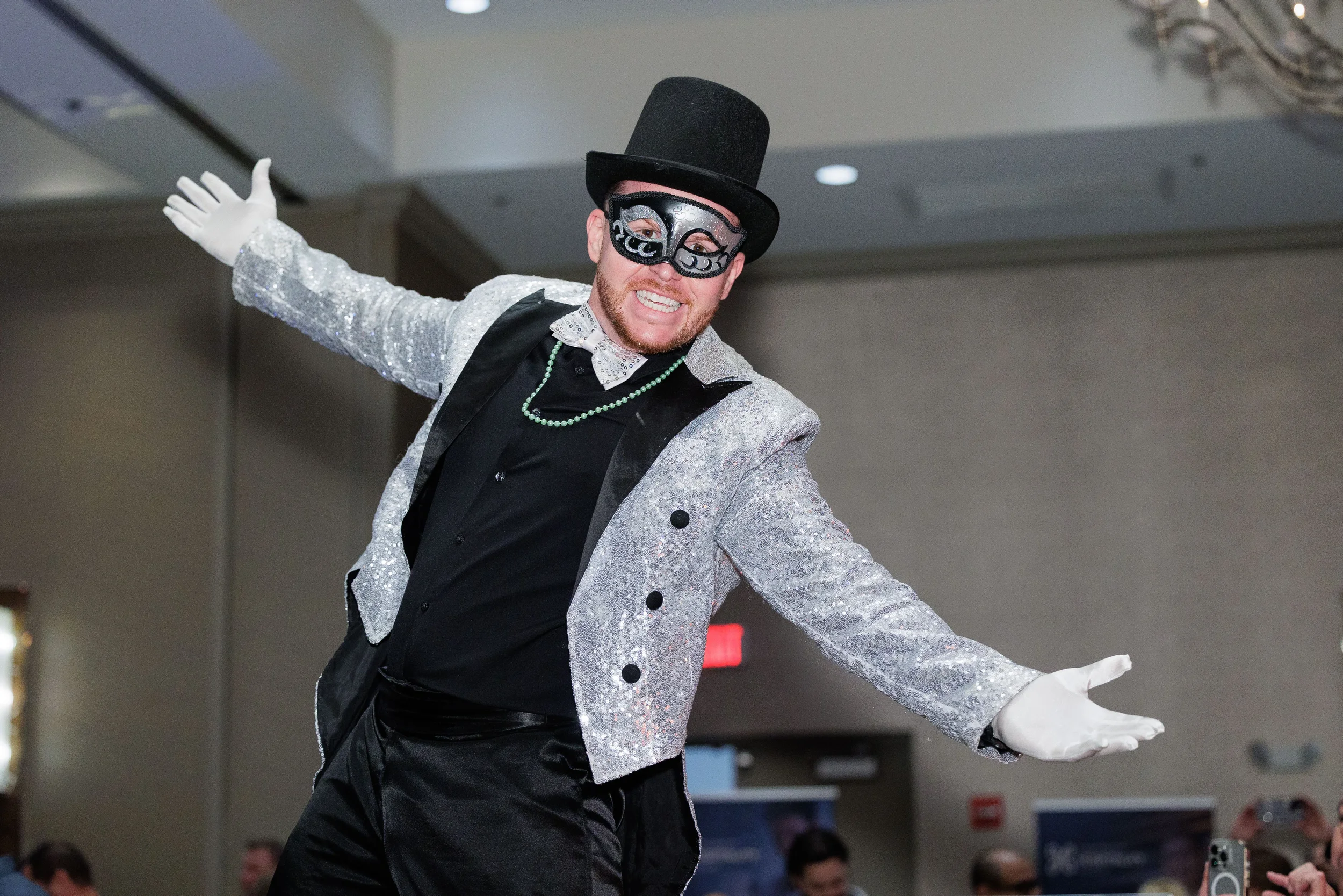 Sequin-jacketed masked performer in top hat spreads arms wide at Orlando corporate conference reception