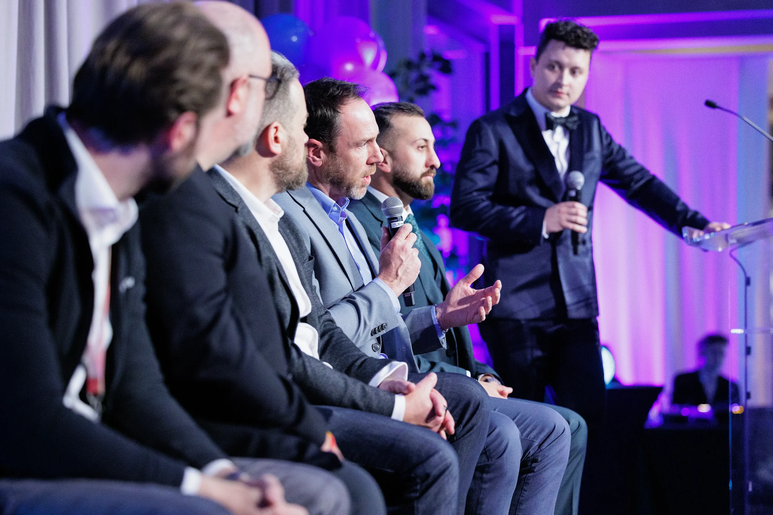 Panelist gestures while speaking into microphone with moderator at podium at Chicago industry conference