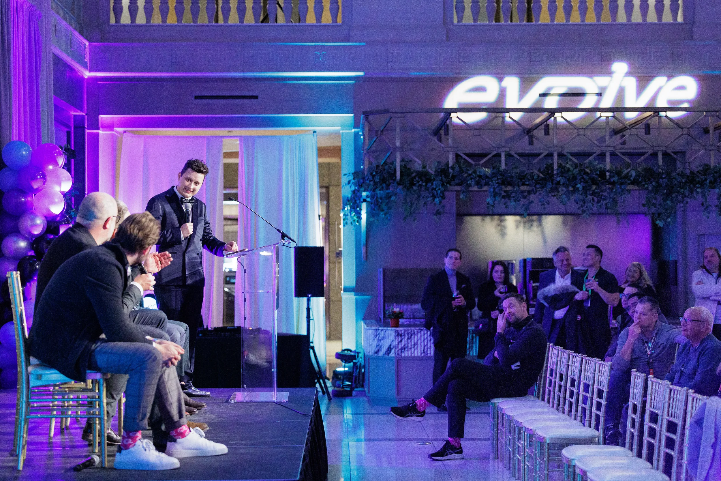 Emcee speaks at podium beside panelists in grand lit venue at Chicago corporate event