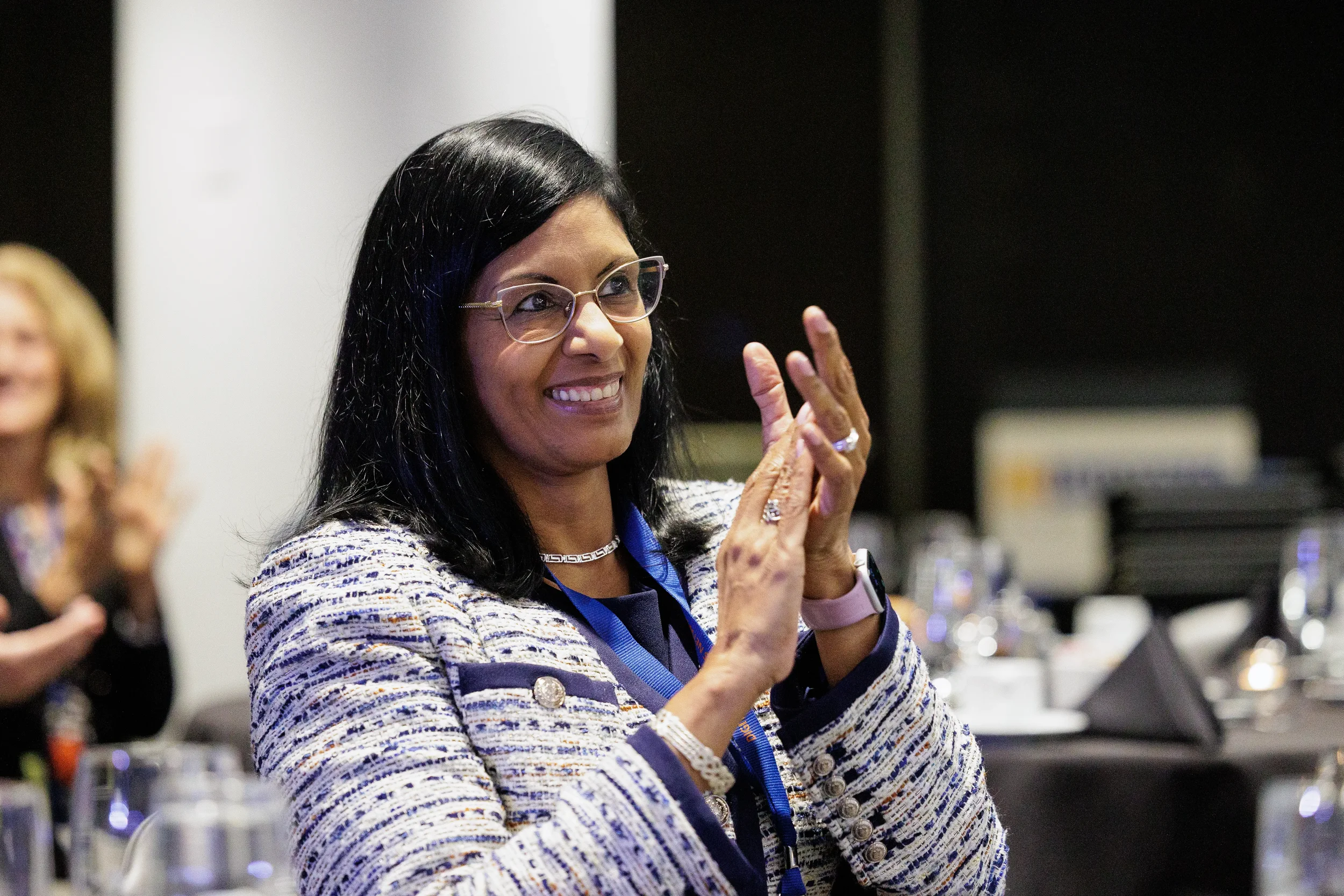 Female attendee with lanyard smiles and applauds at Chicago corporate conference evening event