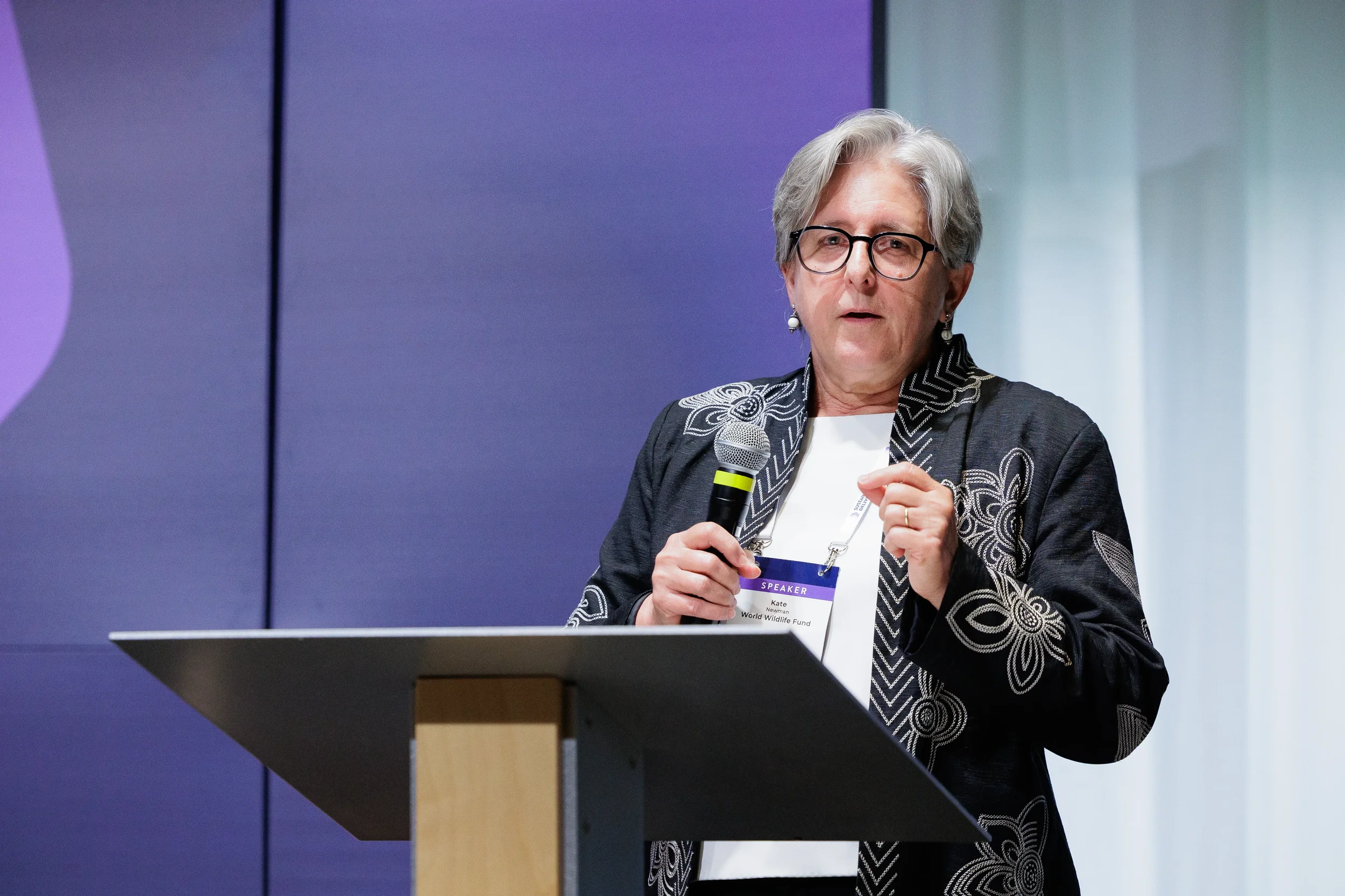 Speaker gestures while presenting from podium with purple lighting at Chicago industry summit