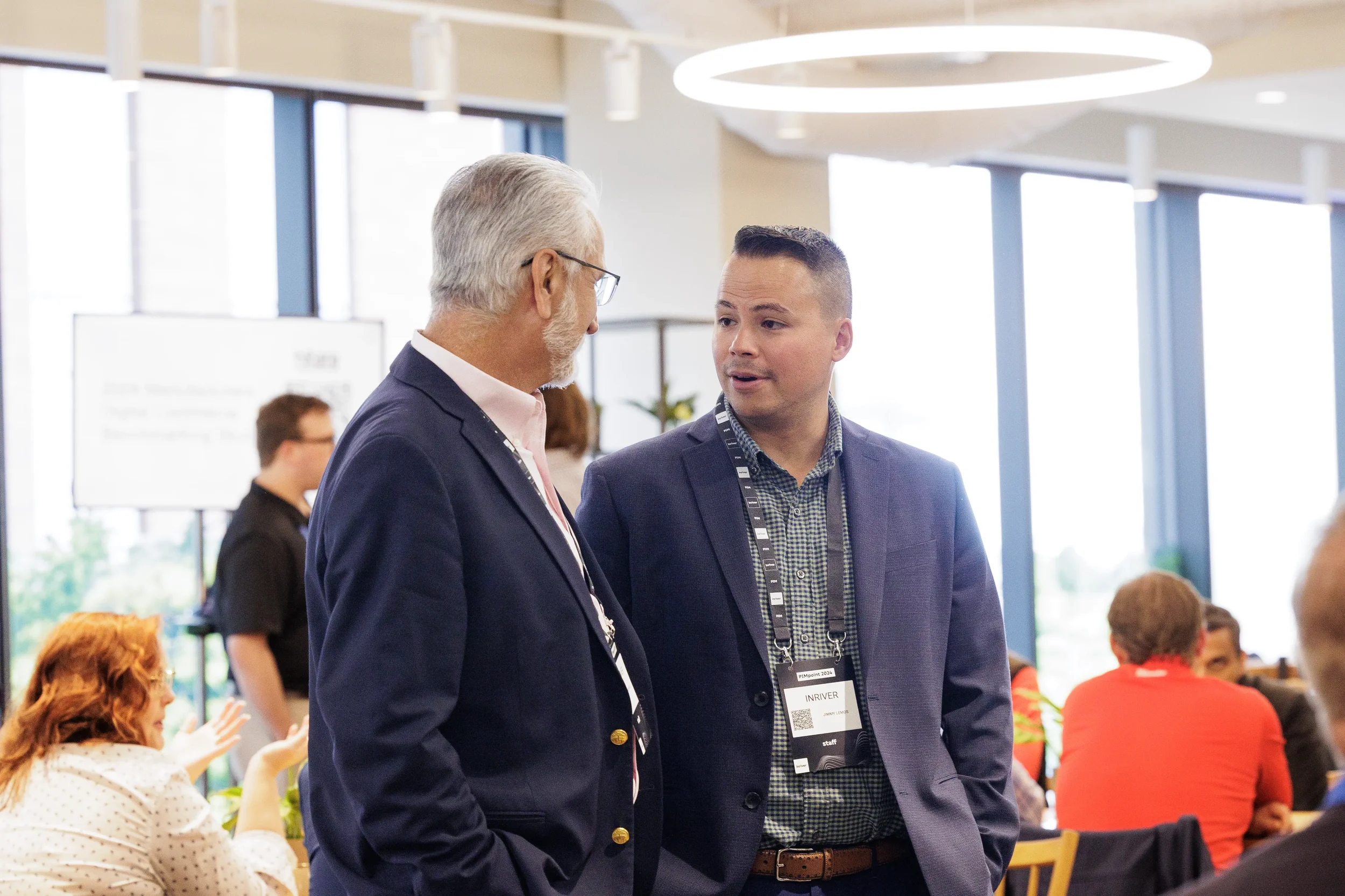 Two attendees in blazers talk during networking break in bright lounge at Orlando conference