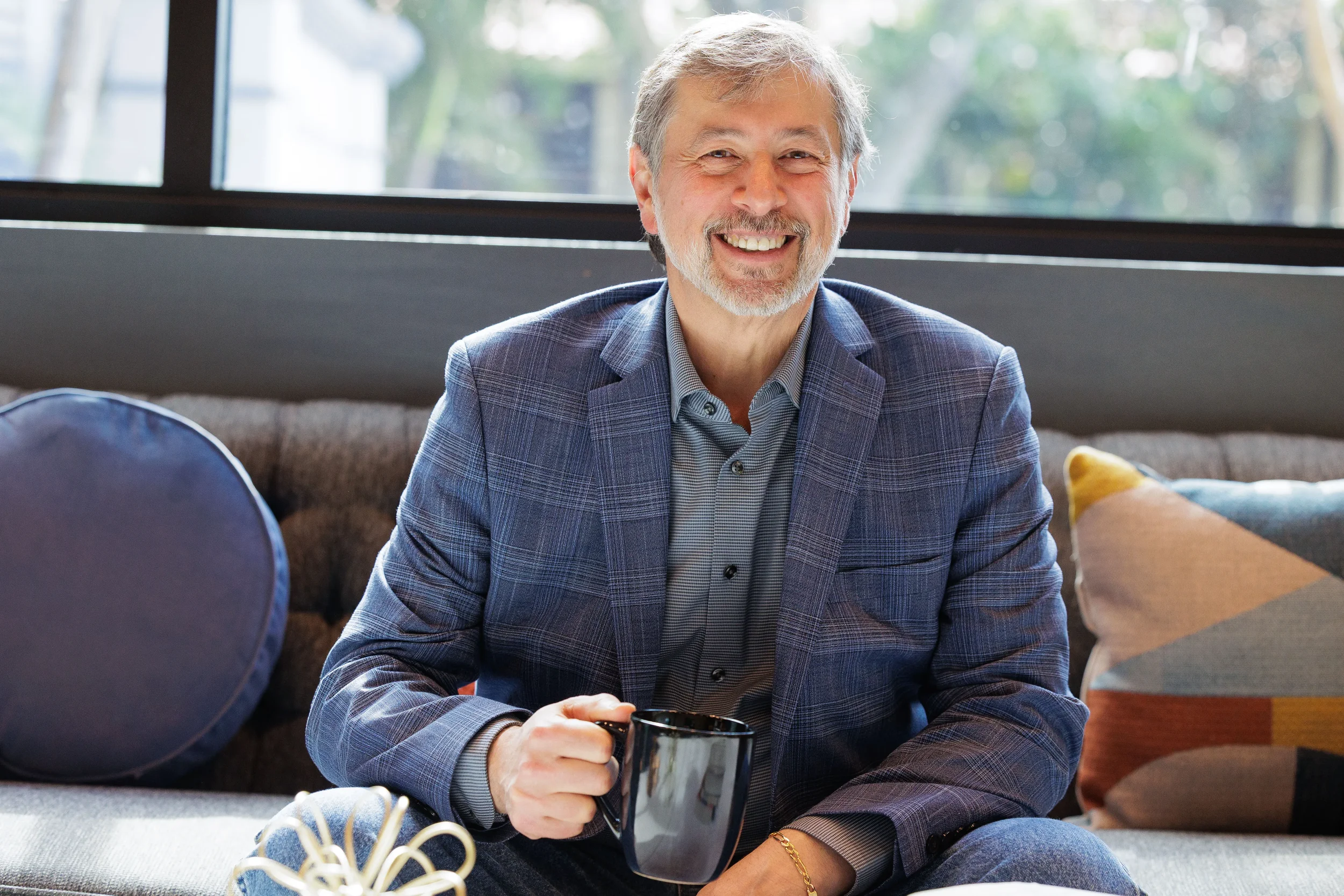 Smiling male attendee holds coffee mug while relaxing on hotel lounge sofa at Orlando corporate event