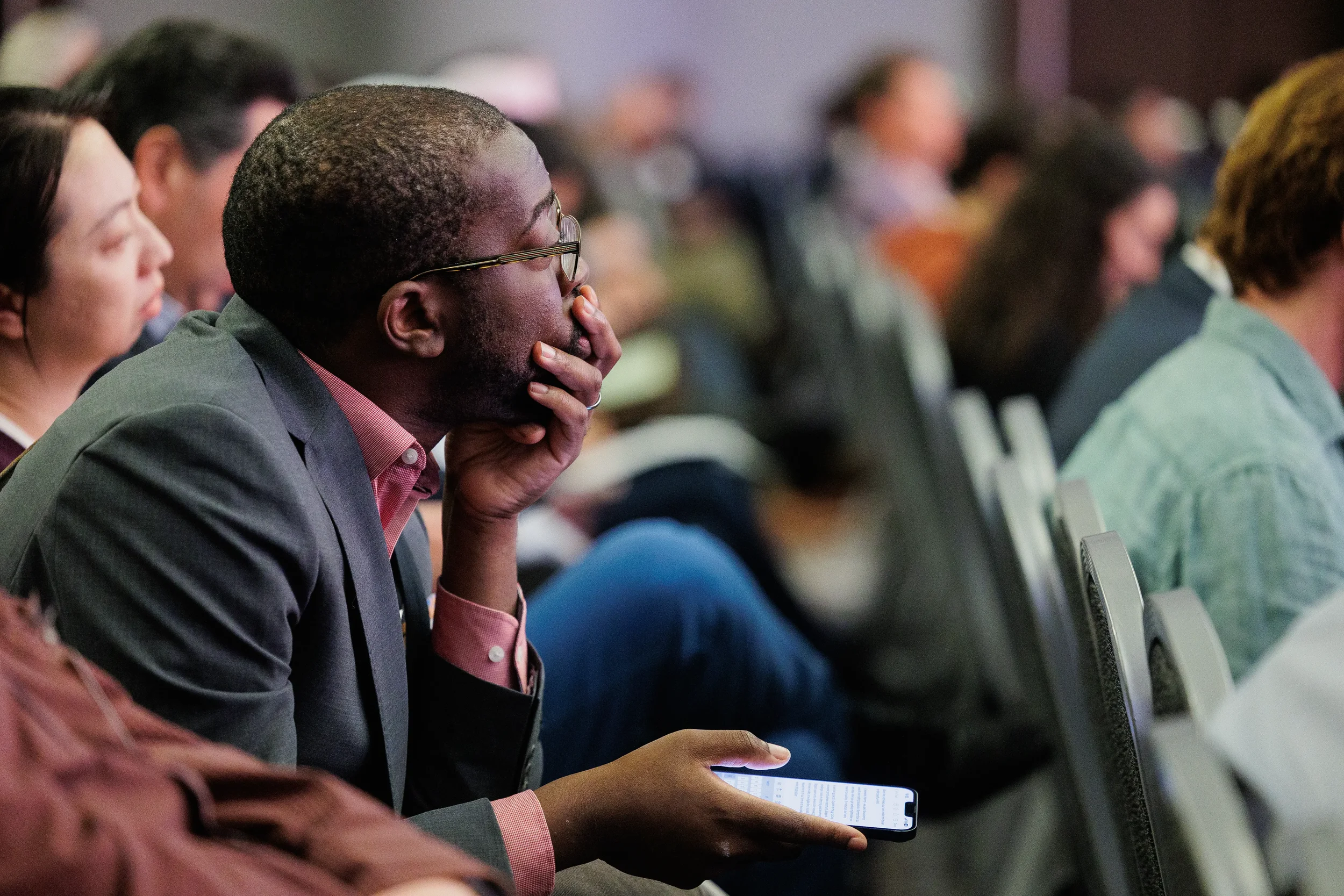 Badged attendee listens intently with phone in hand during session at Chicago industry conference