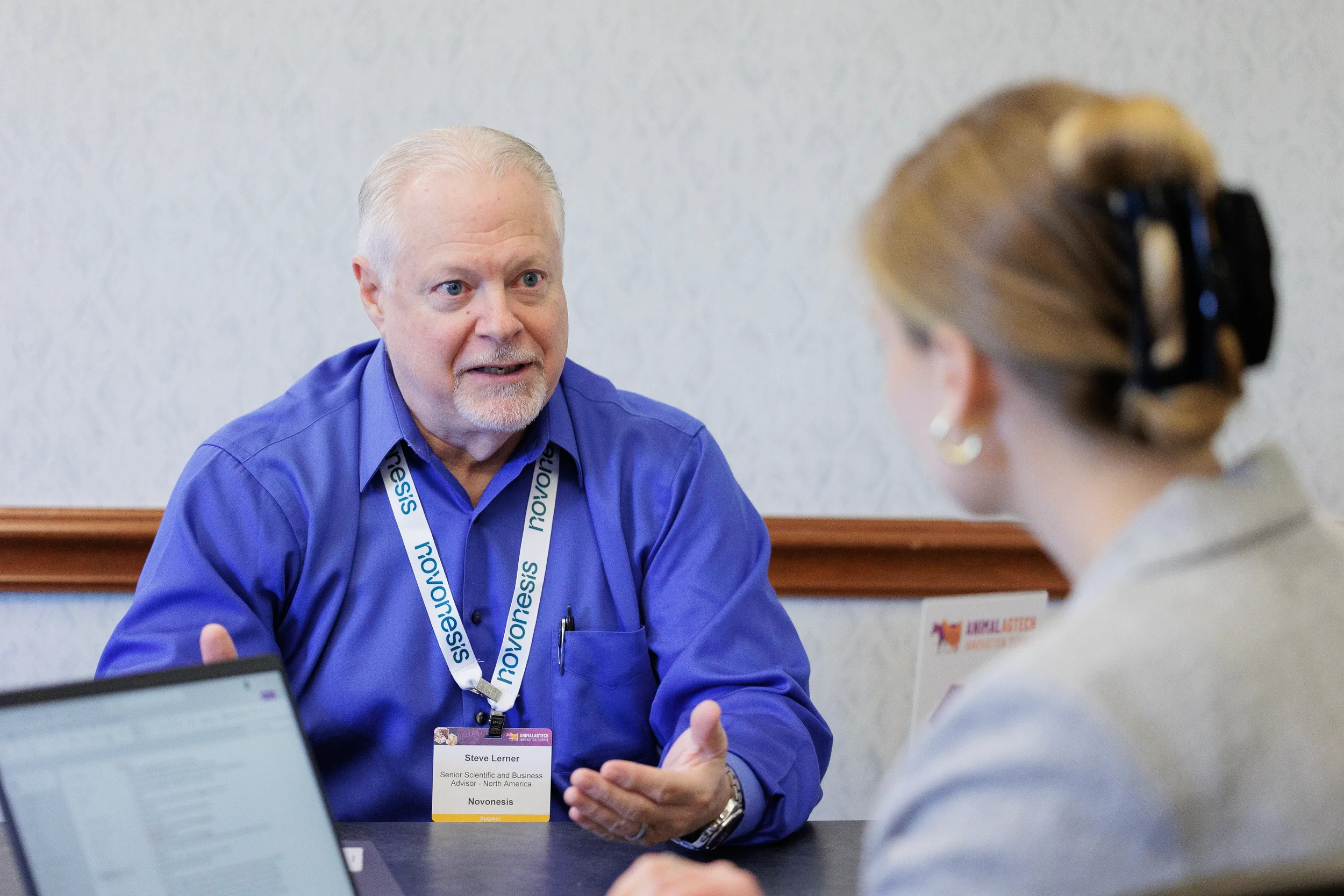 Two attendees converse near laptop during meeting at Orlando corporate conference