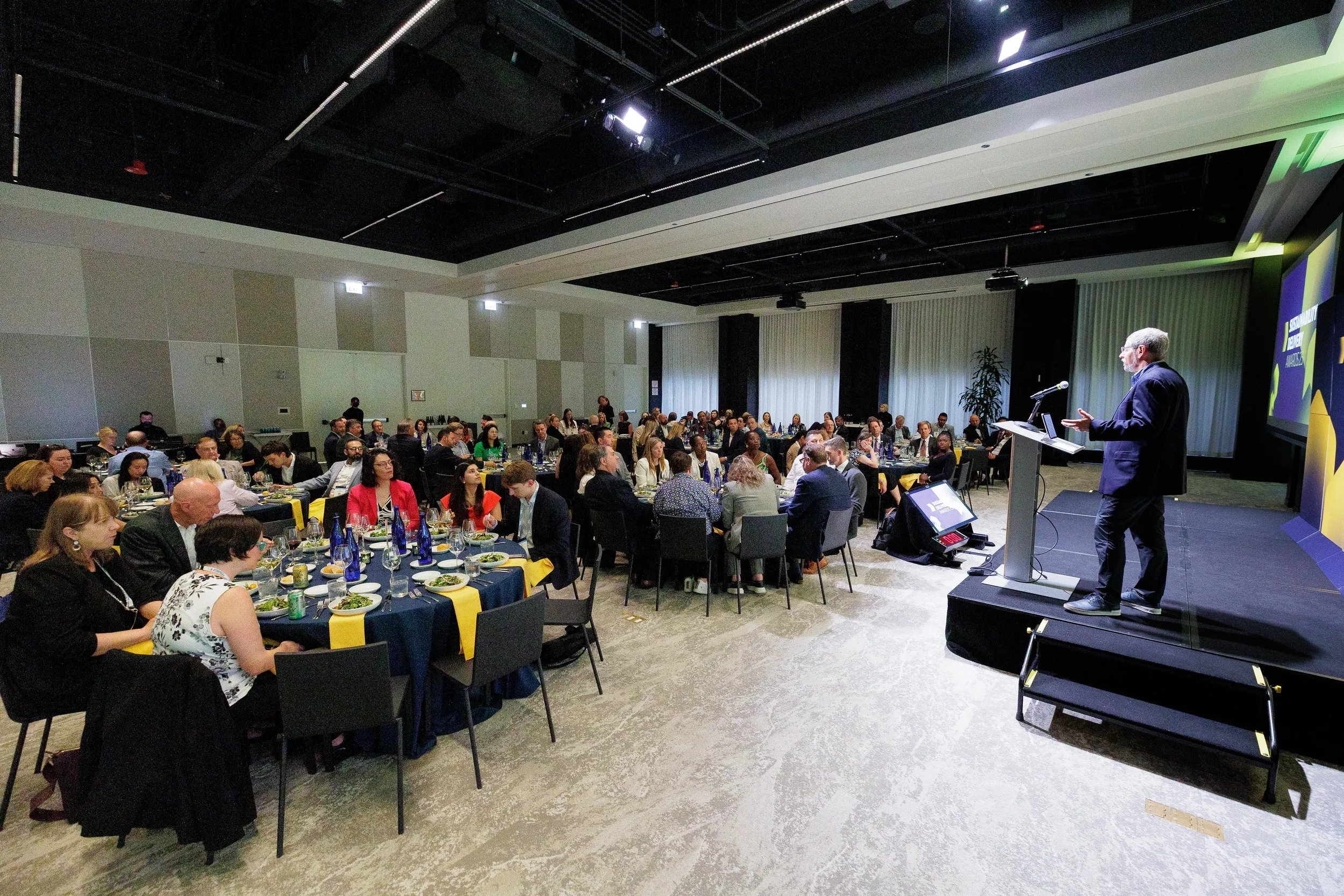 Host addresses seated audience from podium during Orlando corporate awards dinner