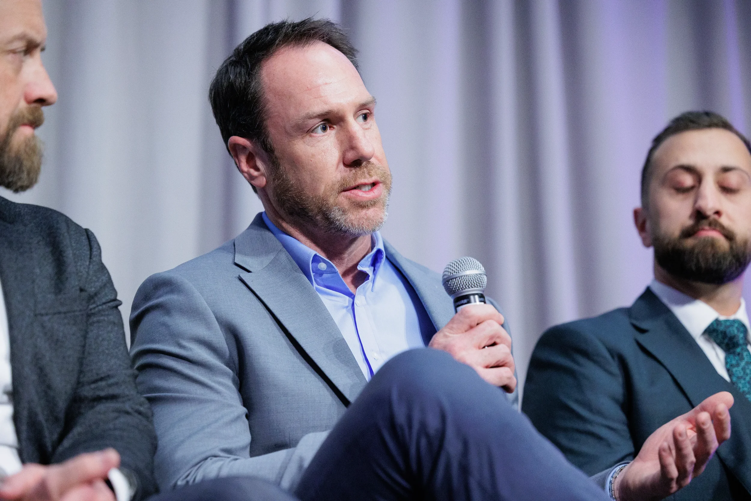 Panelist in blue blazer speaks into microphone during seated panel discussion at Orlando corporate event