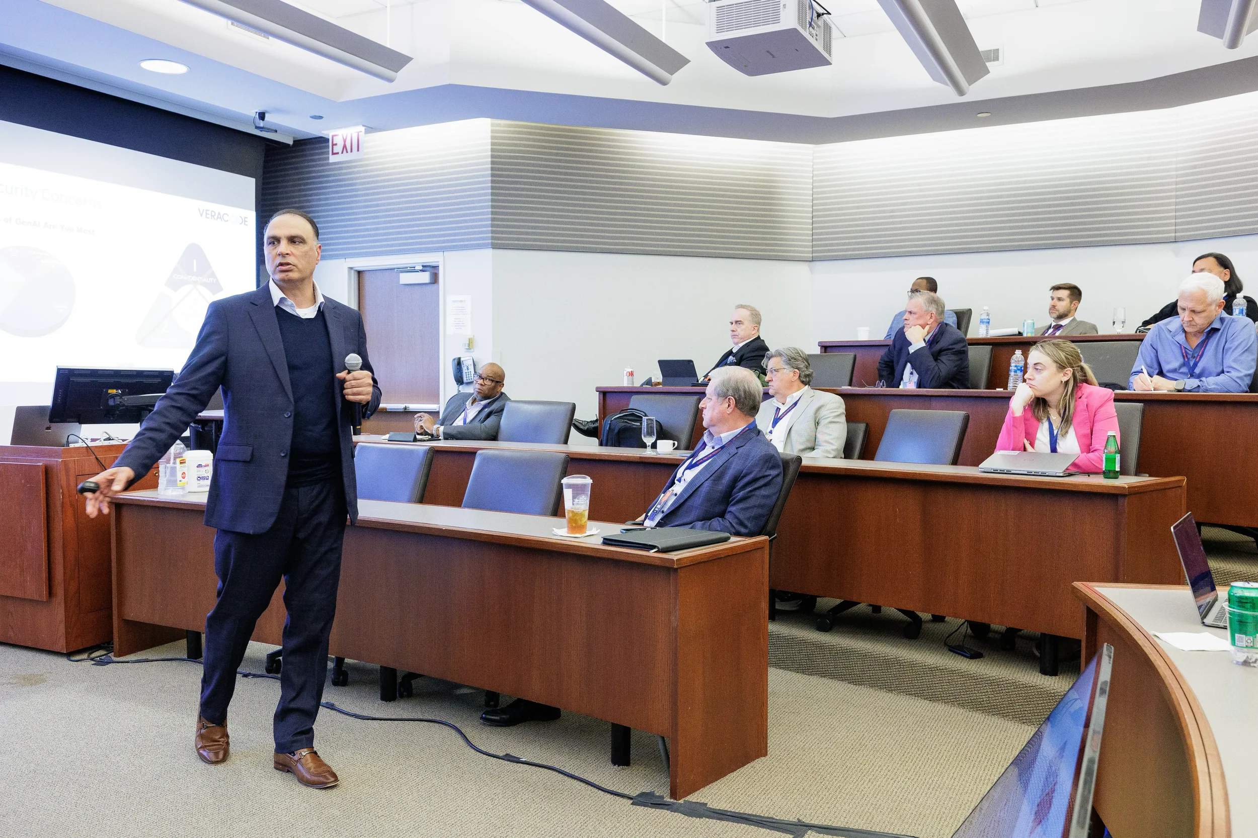 Male speaker holds microphone and gestures to attendees in tiered room at Chicago industry conference